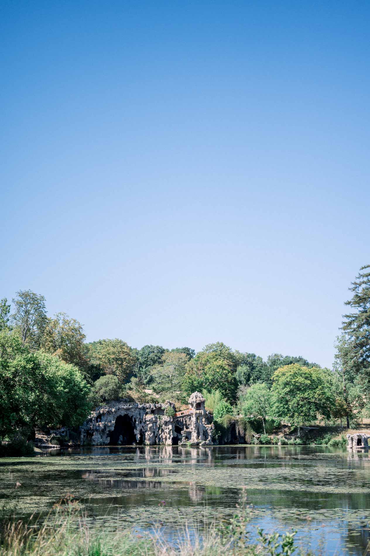 Lake and grotto of Parc Majolan surrounded by greenery under a blue sky