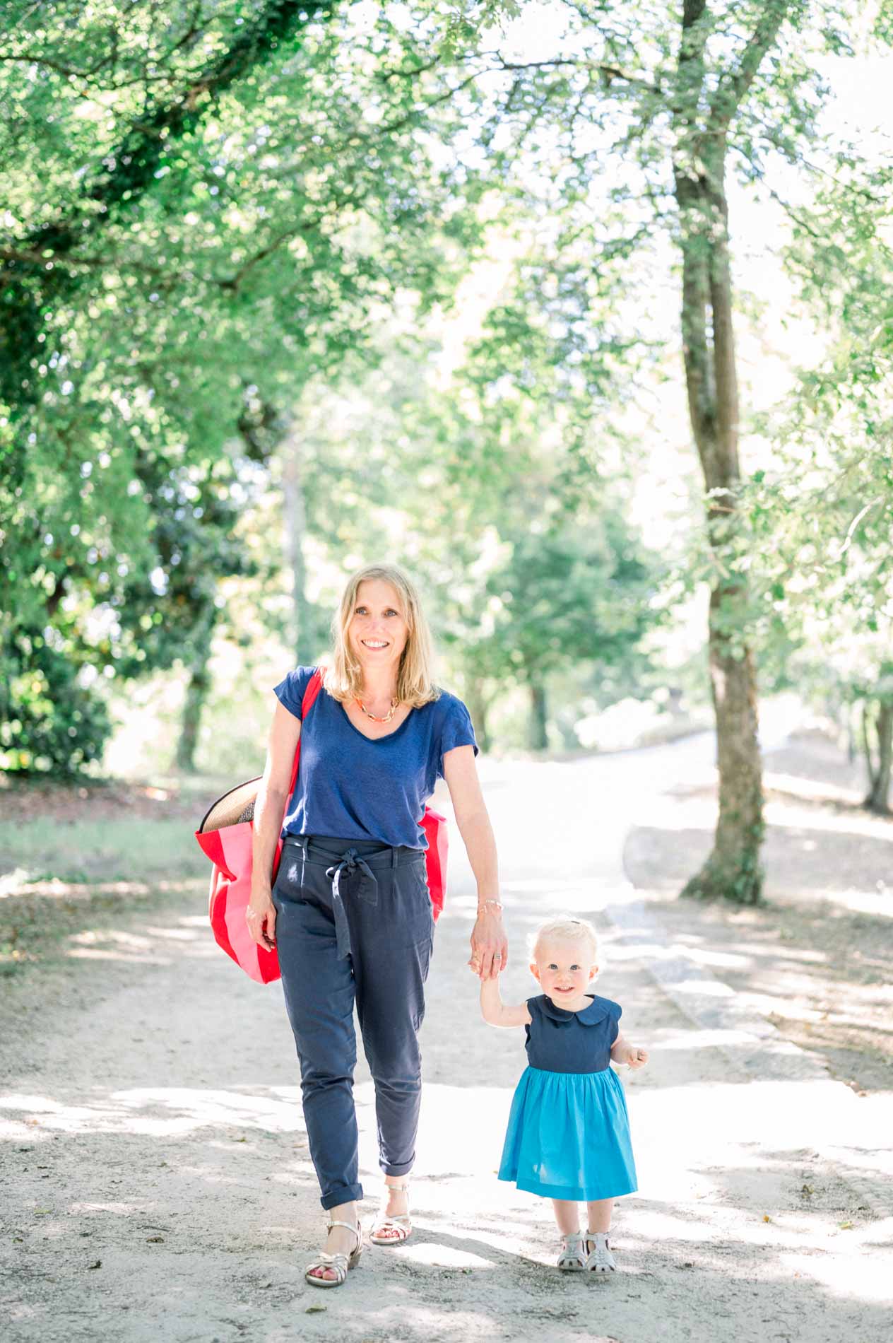Mum and her little daughter walking hand in hand along a shady path