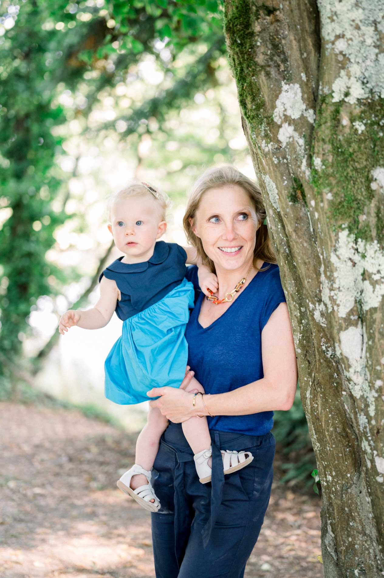Mum holding her daughter in a blue dress against an ivy-covered tree
