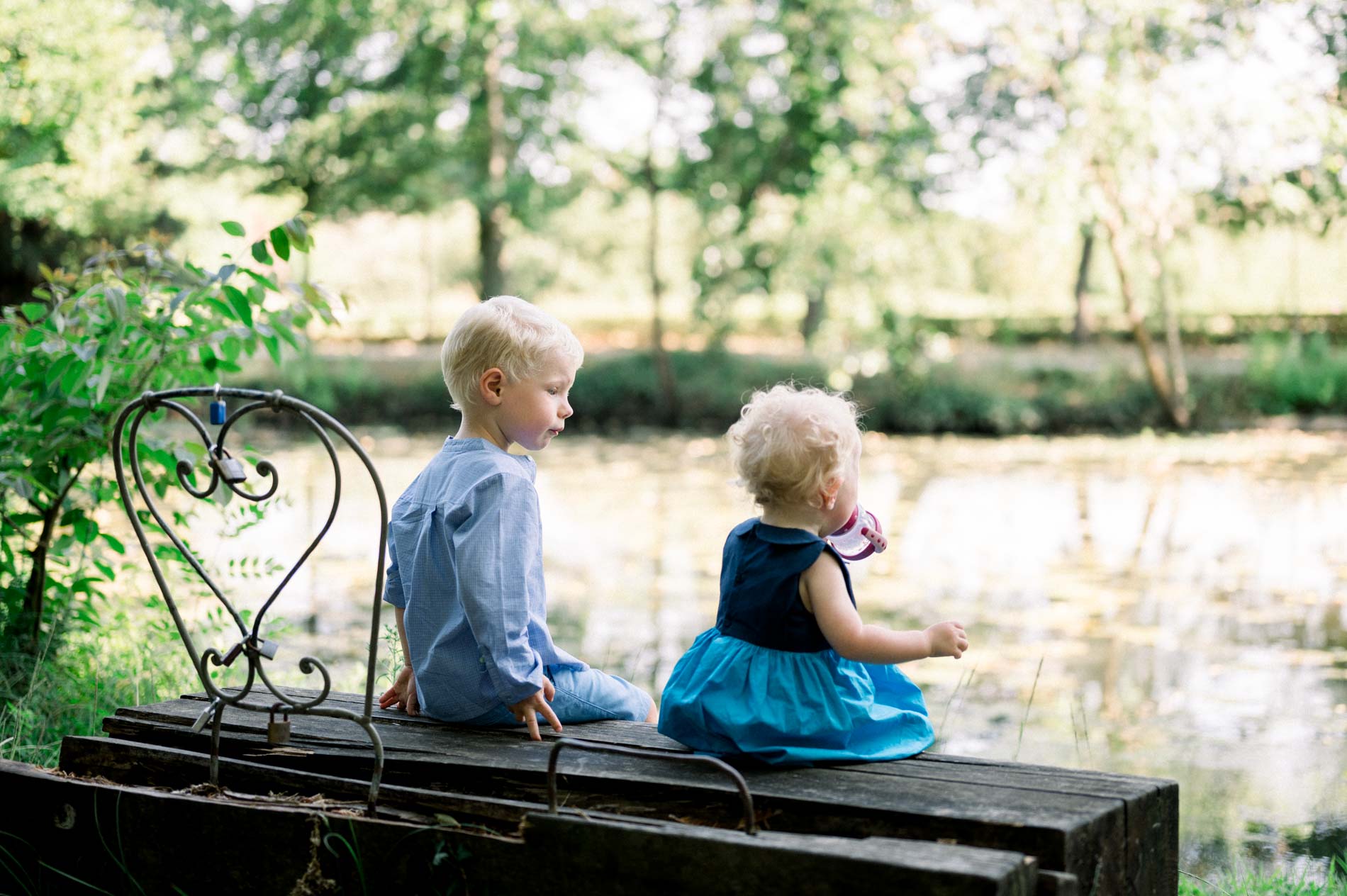 Brother and sister sitting on a bench by the lake in Parc Majolan, seen from behind