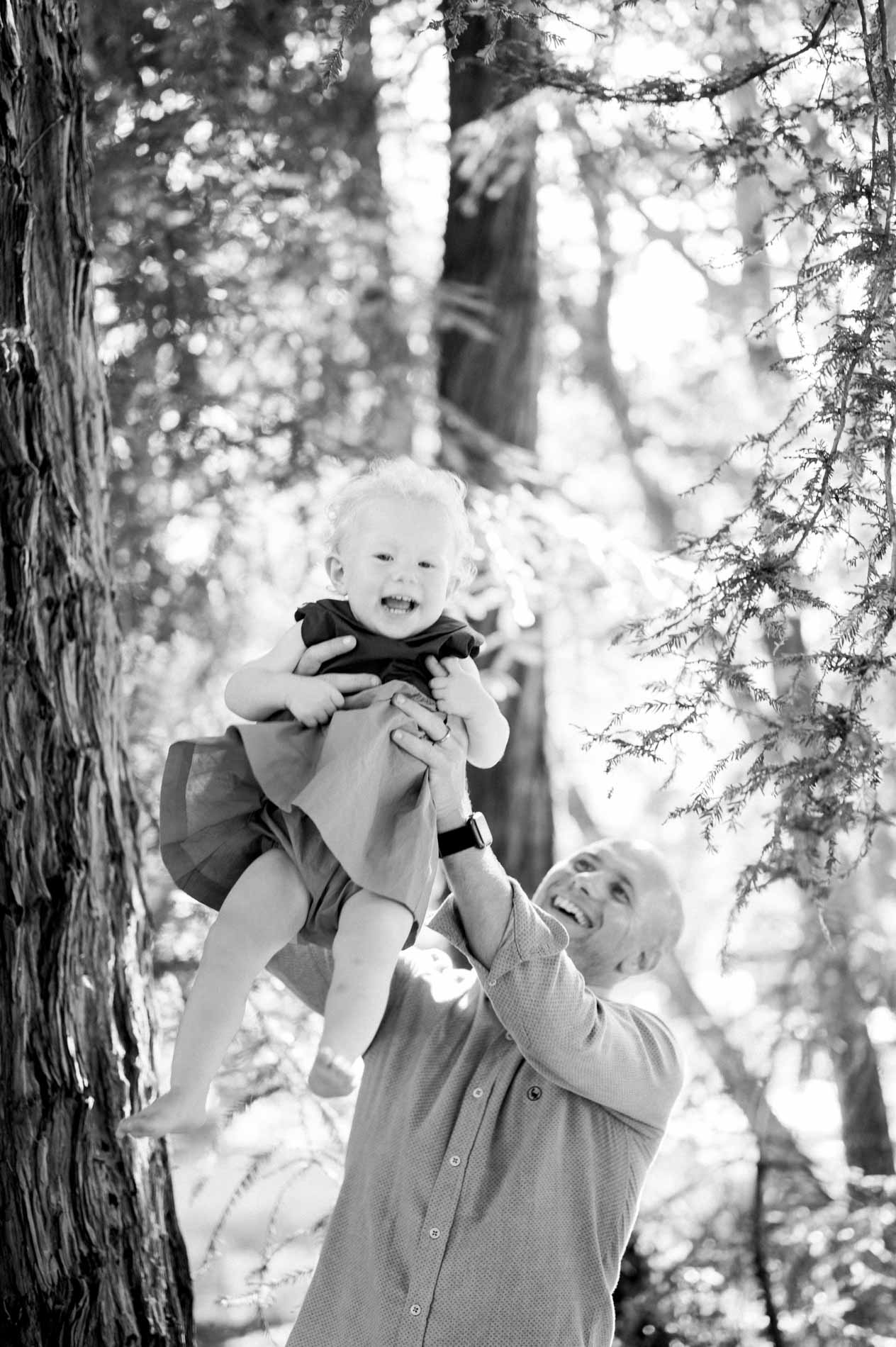 Dad lifting his daughter high in the air under the trees, in black and white