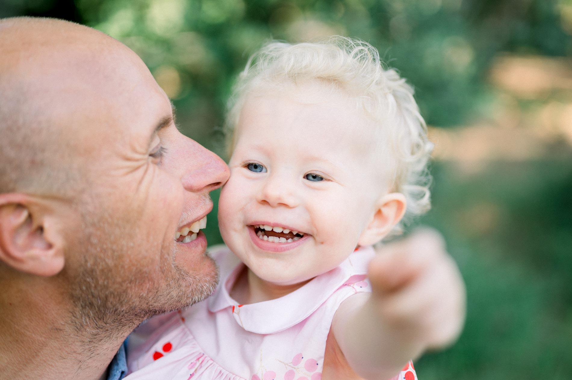 Dad nose to nose with his giggling daughter in a pink dress