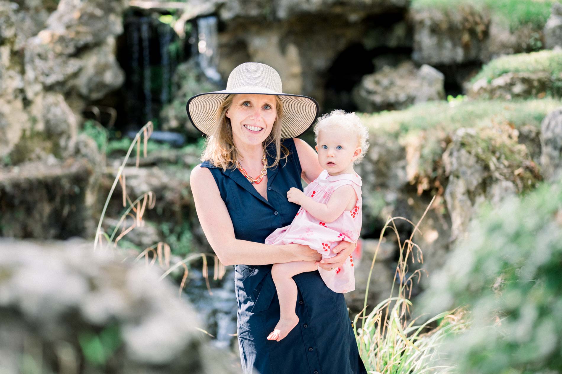 Mum in a hat holding her daughter in front of the grotto waterfall