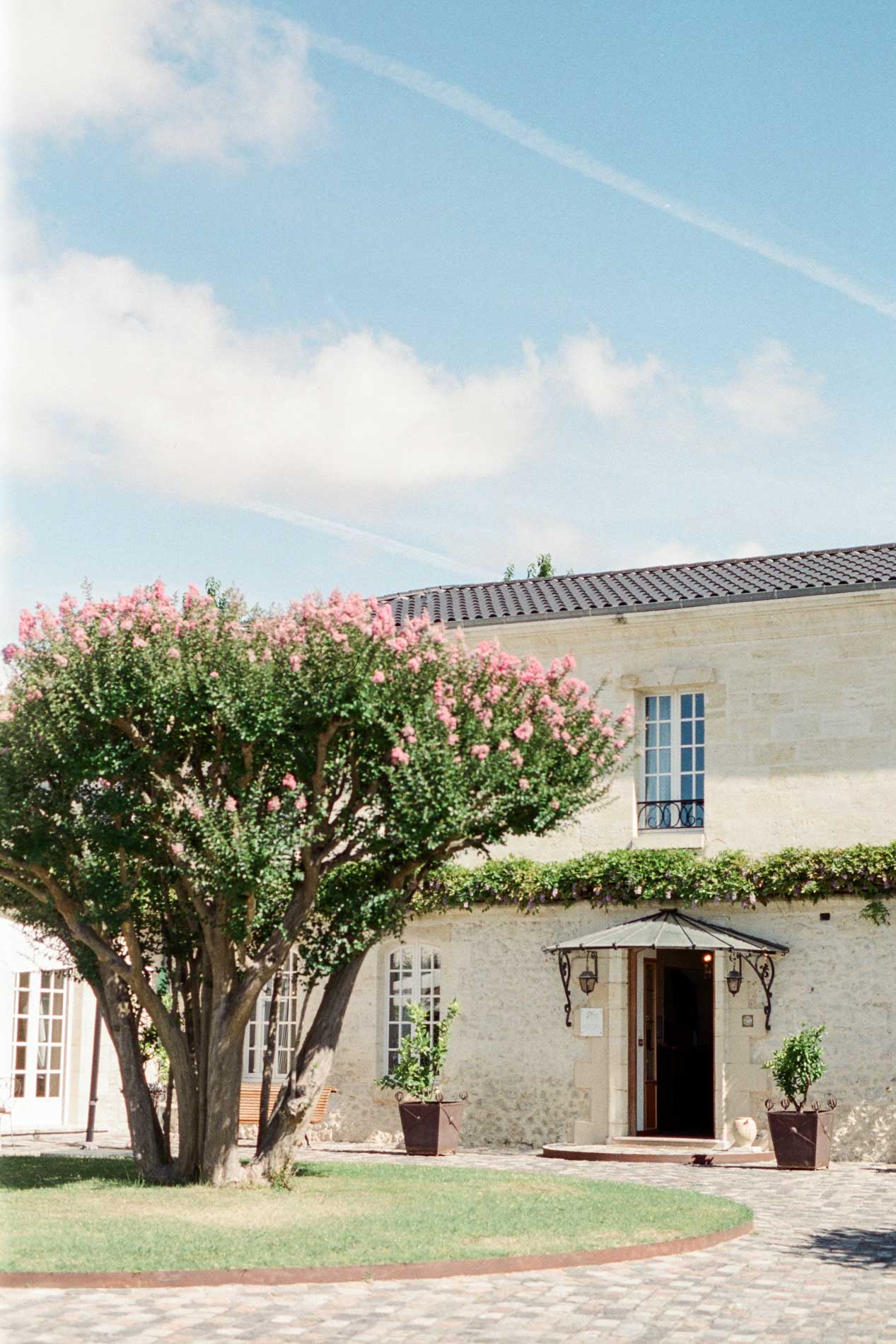 Façade en pierre du Domaine de Larchey et lagerstroemia en fleurs sous un ciel bleu