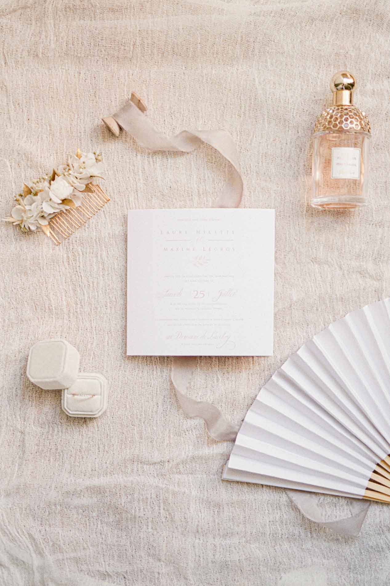 Faire-part, parfum, éventail et peigne fleuri de la mariée posés sur un drap de lin