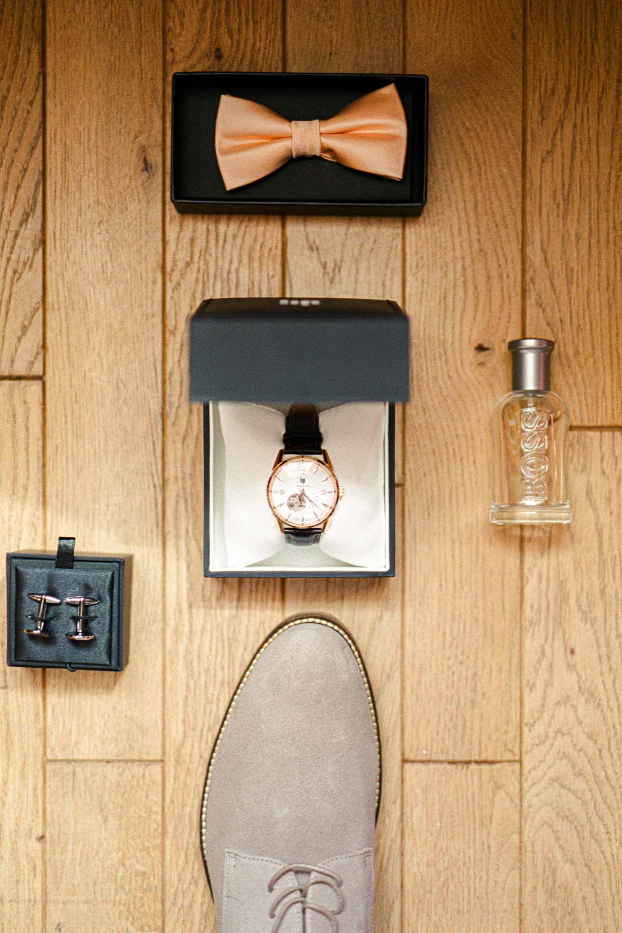 Nœud papillon pêche, montre, parfum et chaussure du marié sur un parquet en bois