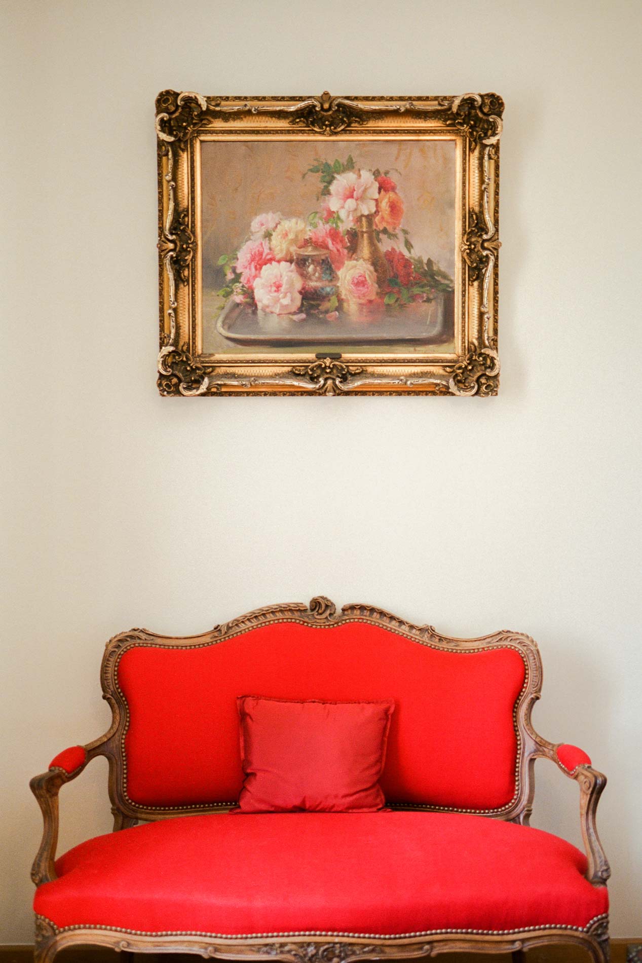 Canapé de style Louis XV rouge sous un tableau de fleurs au cadre doré