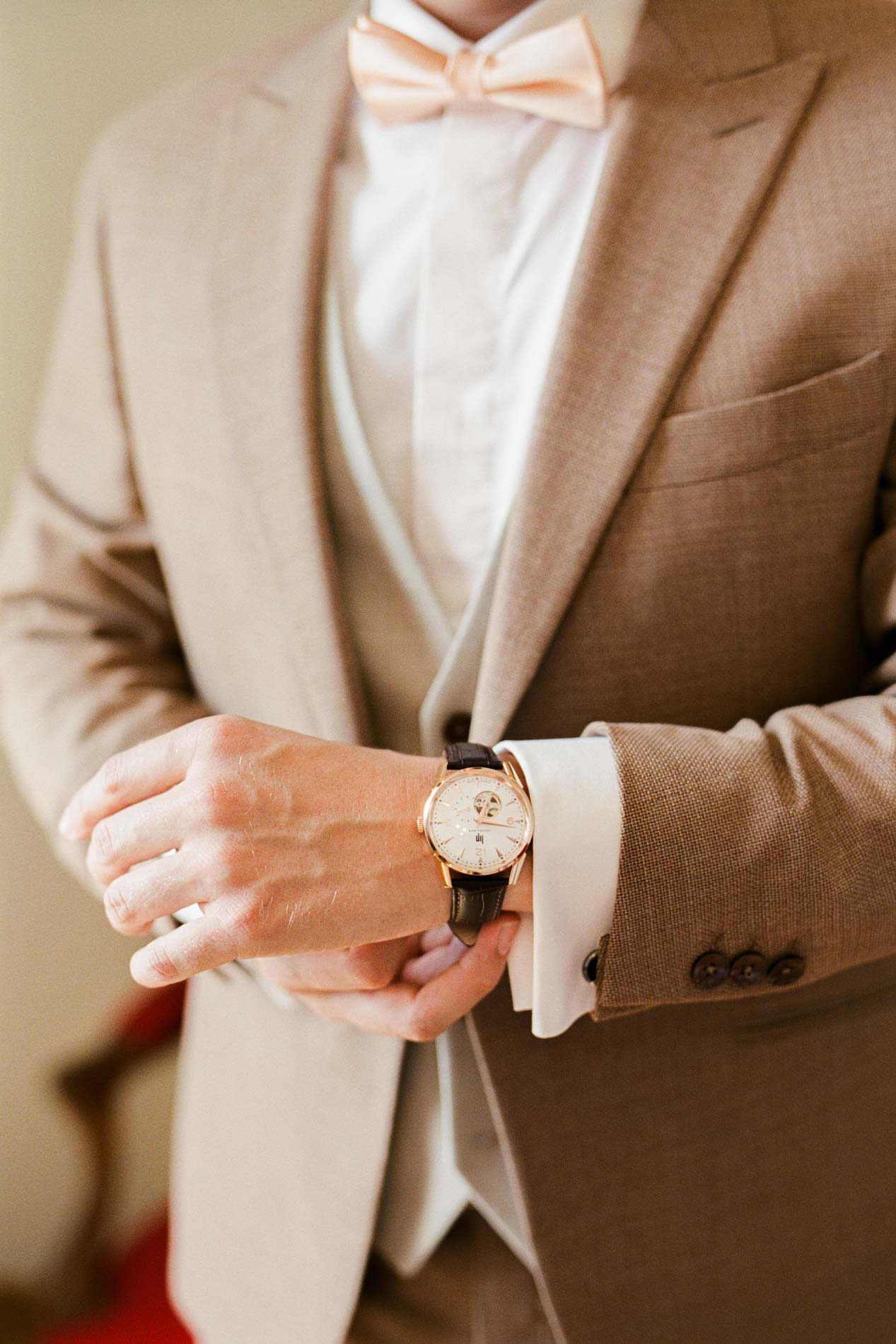 Le marié en veste beige ajuste sa montre pendant ses préparatifs