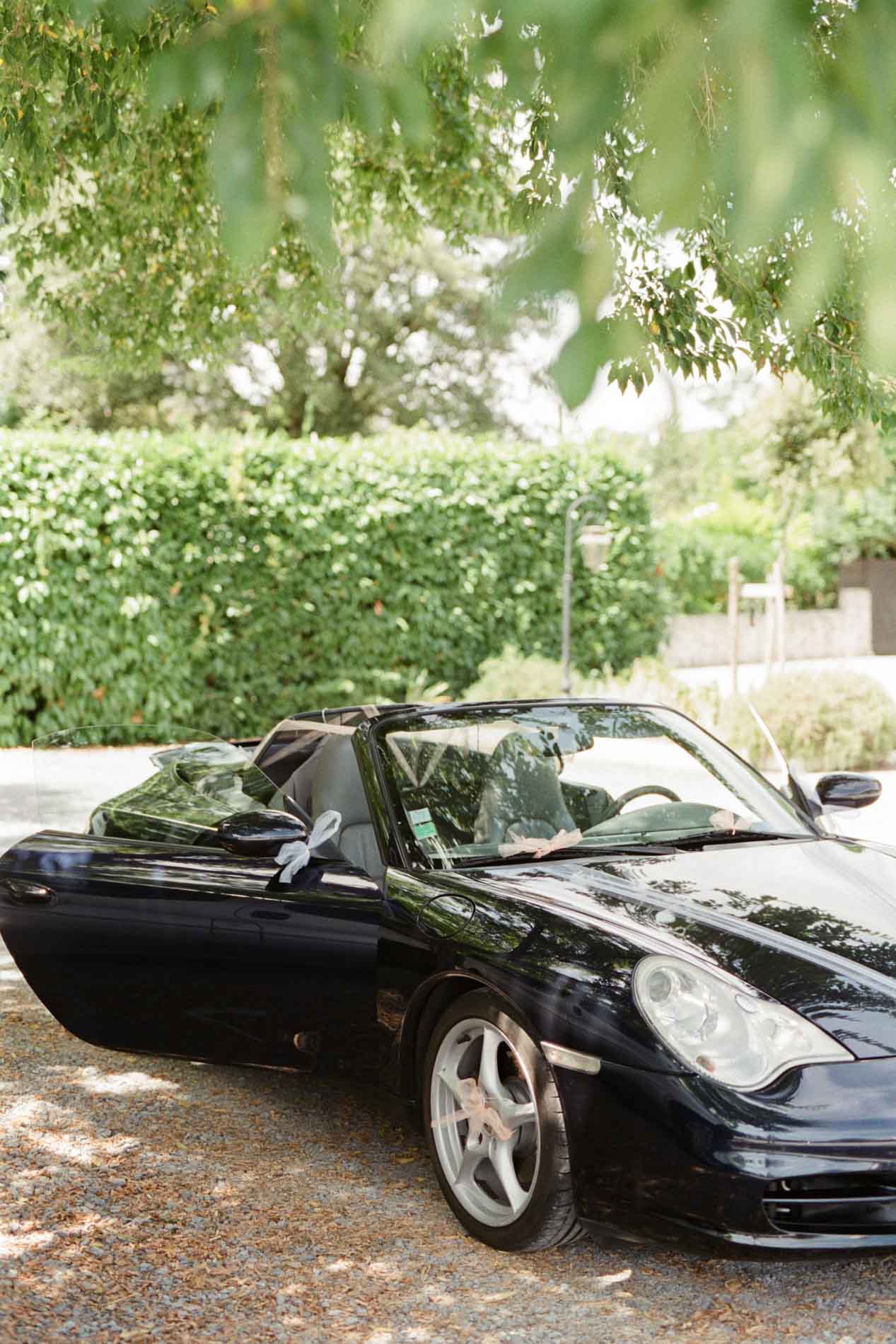 Porsche 911 noire décapotable garée sous les arbres pour le mariage au Domaine de Larchey