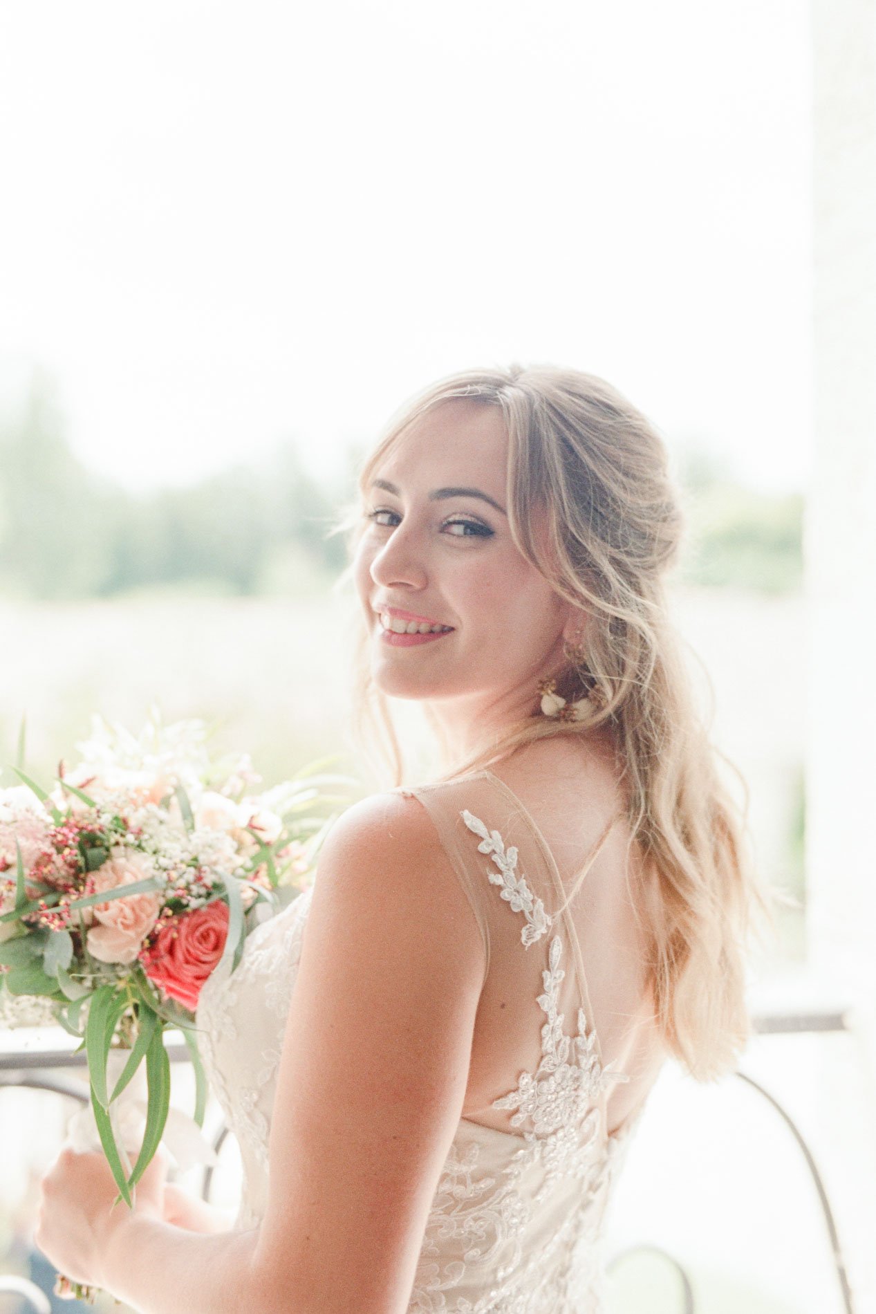 Portrait de la mariée souriante tenant son bouquet de roses pêche près d'une fenêtre