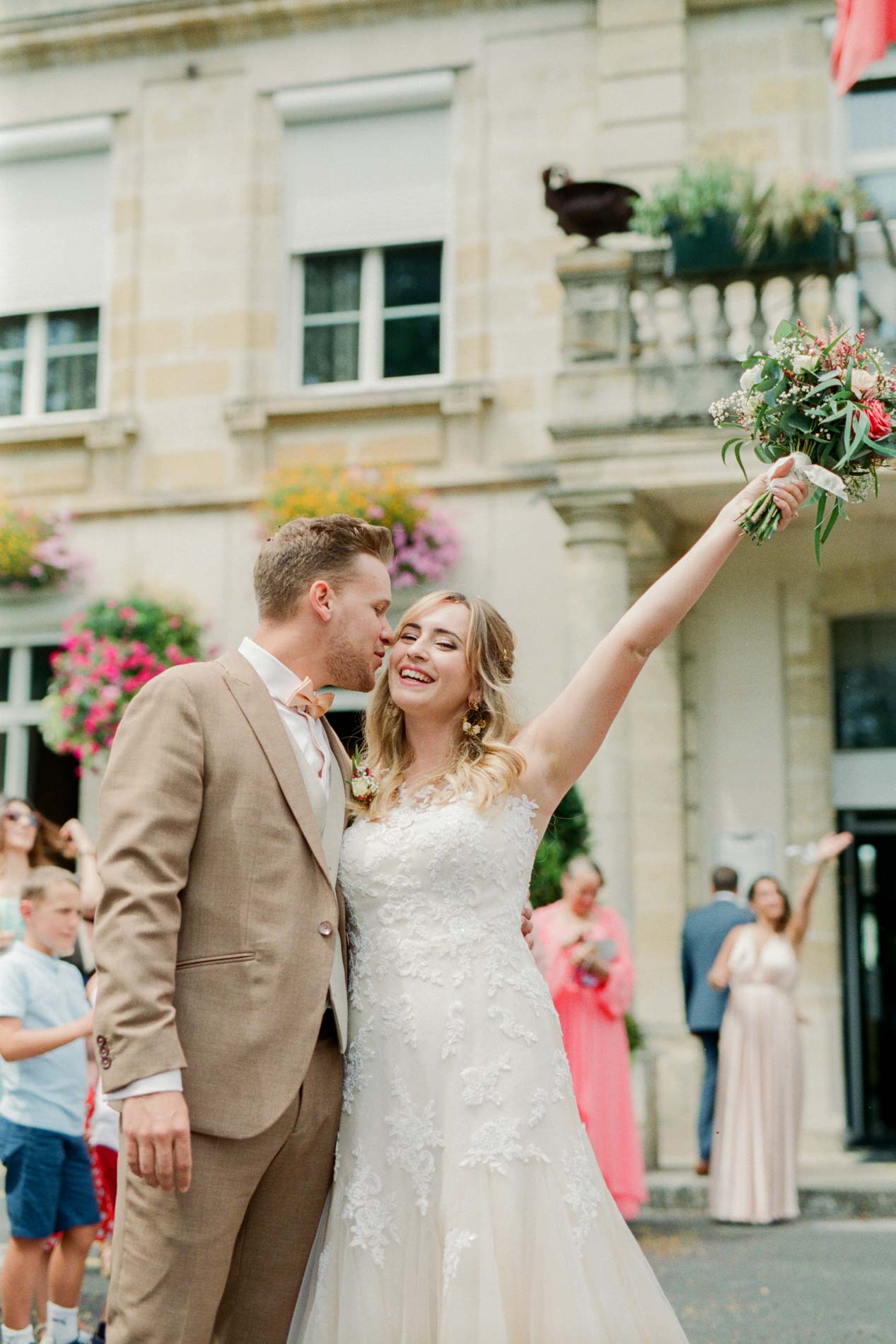 La mariée lève son bouquet en signe de joie devant la mairie