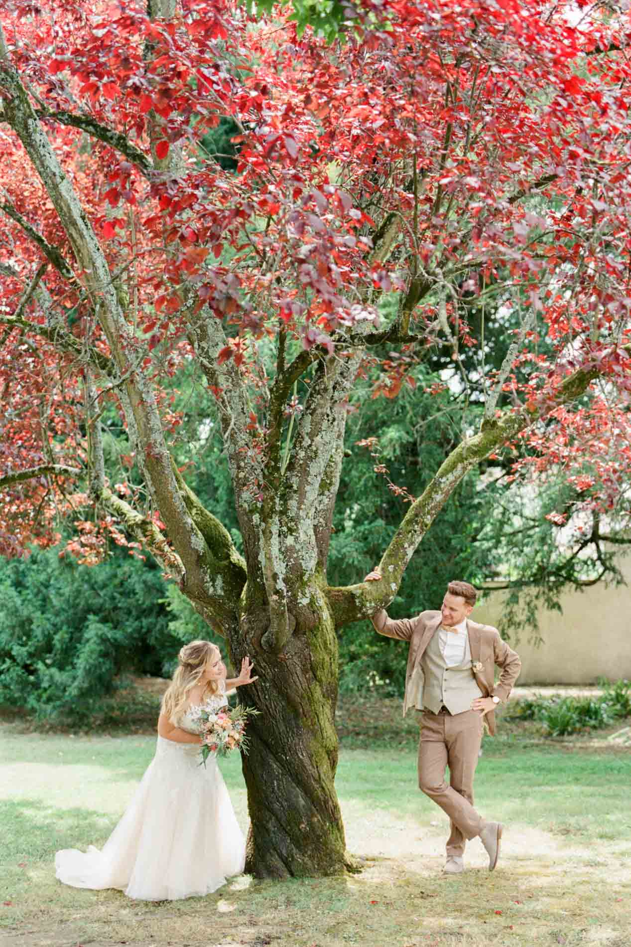 Les mariés de part et d'autre d'un arbre au feuillage pourpre dans un parc