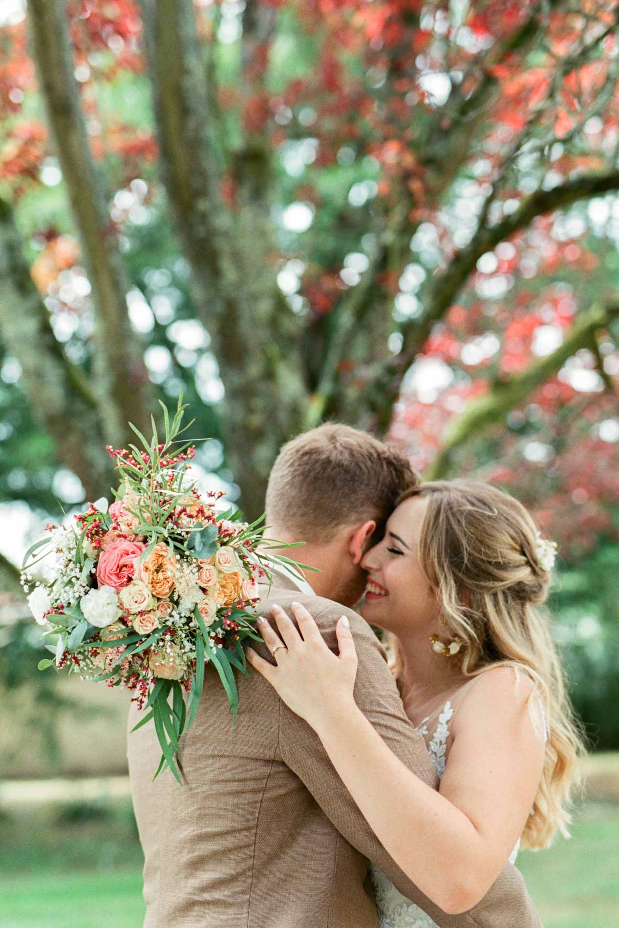 La mariée blottie contre le marié, le bouquet coloré entre eux