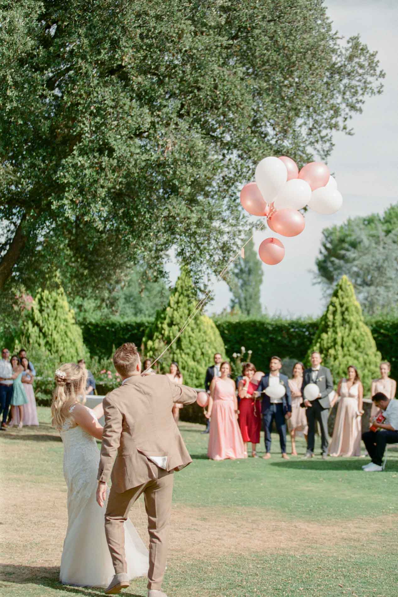 Les mariés regardent s'envoler des ballons roses devant leurs invités