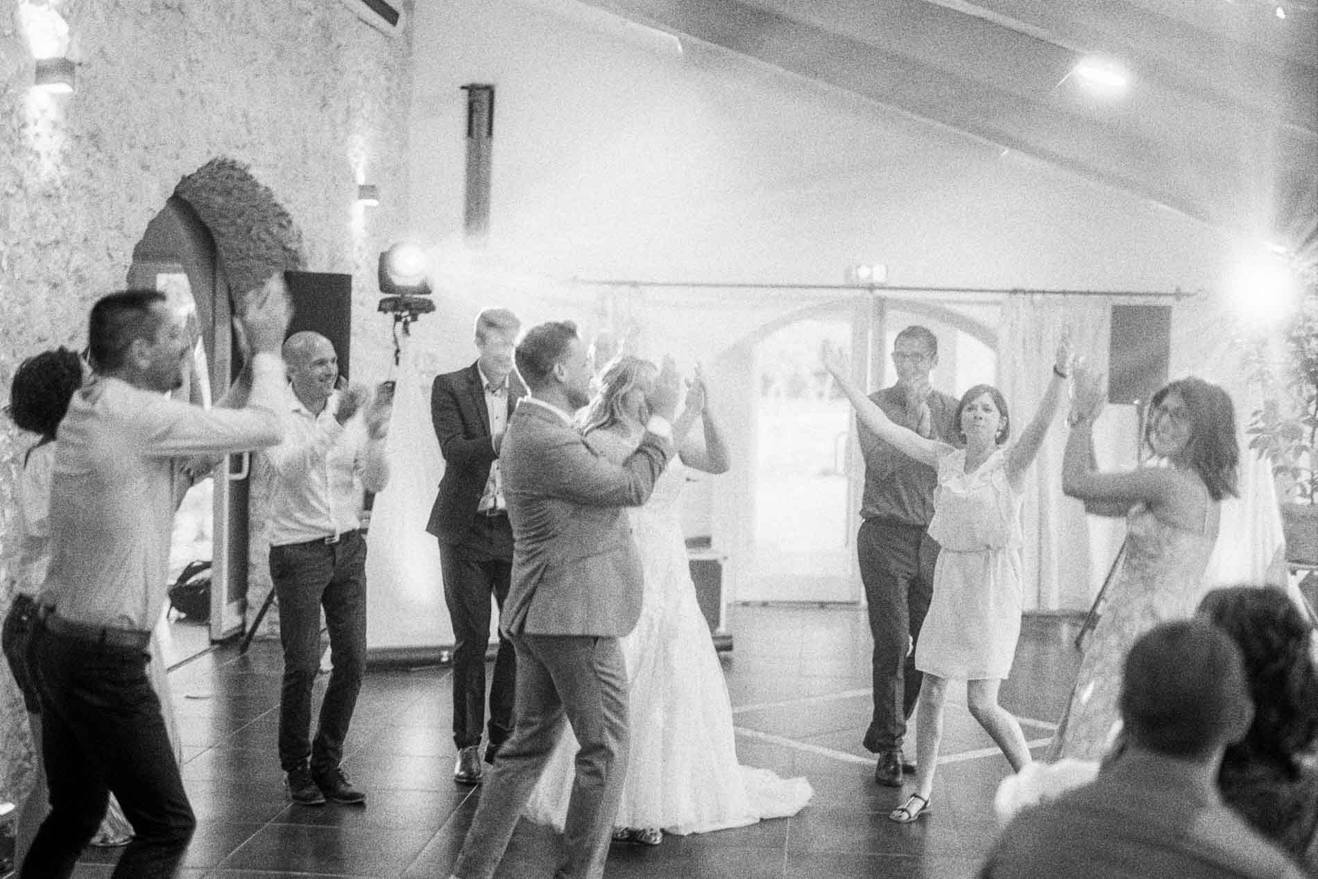 Invités et mariés dansent ensemble pendant la soirée, en noir et blanc