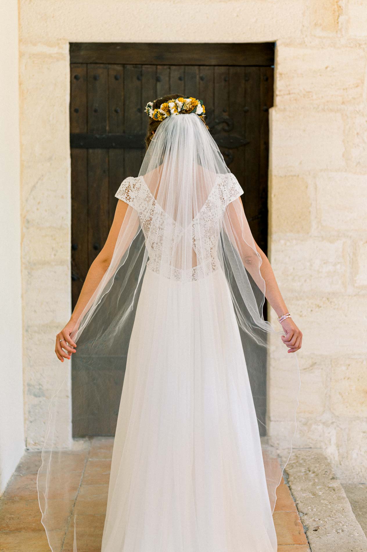 Bride seen from behind spreading her long veil in front of a wooden door