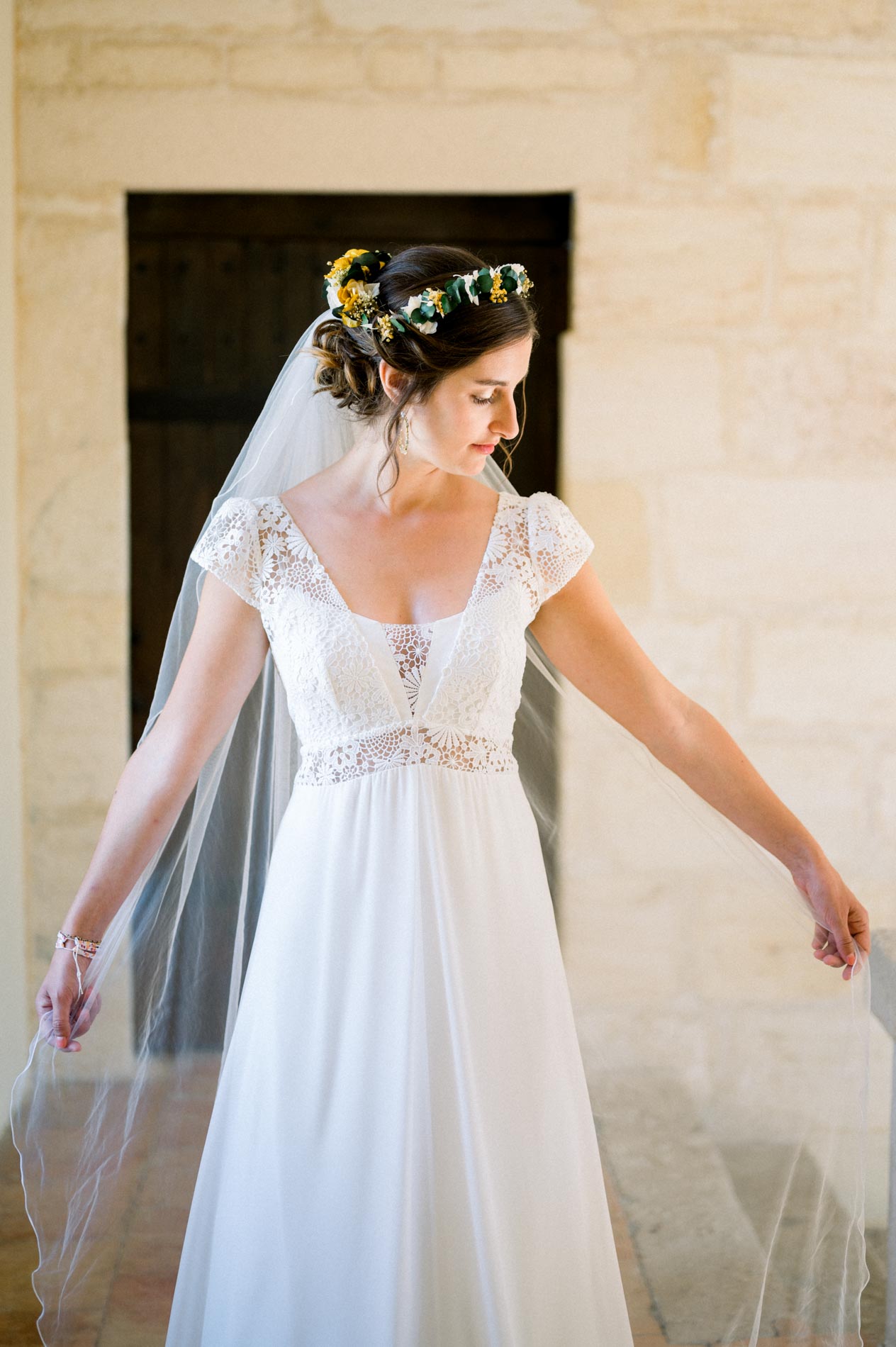 Bride in a lace gown and flower crown holding out her veil