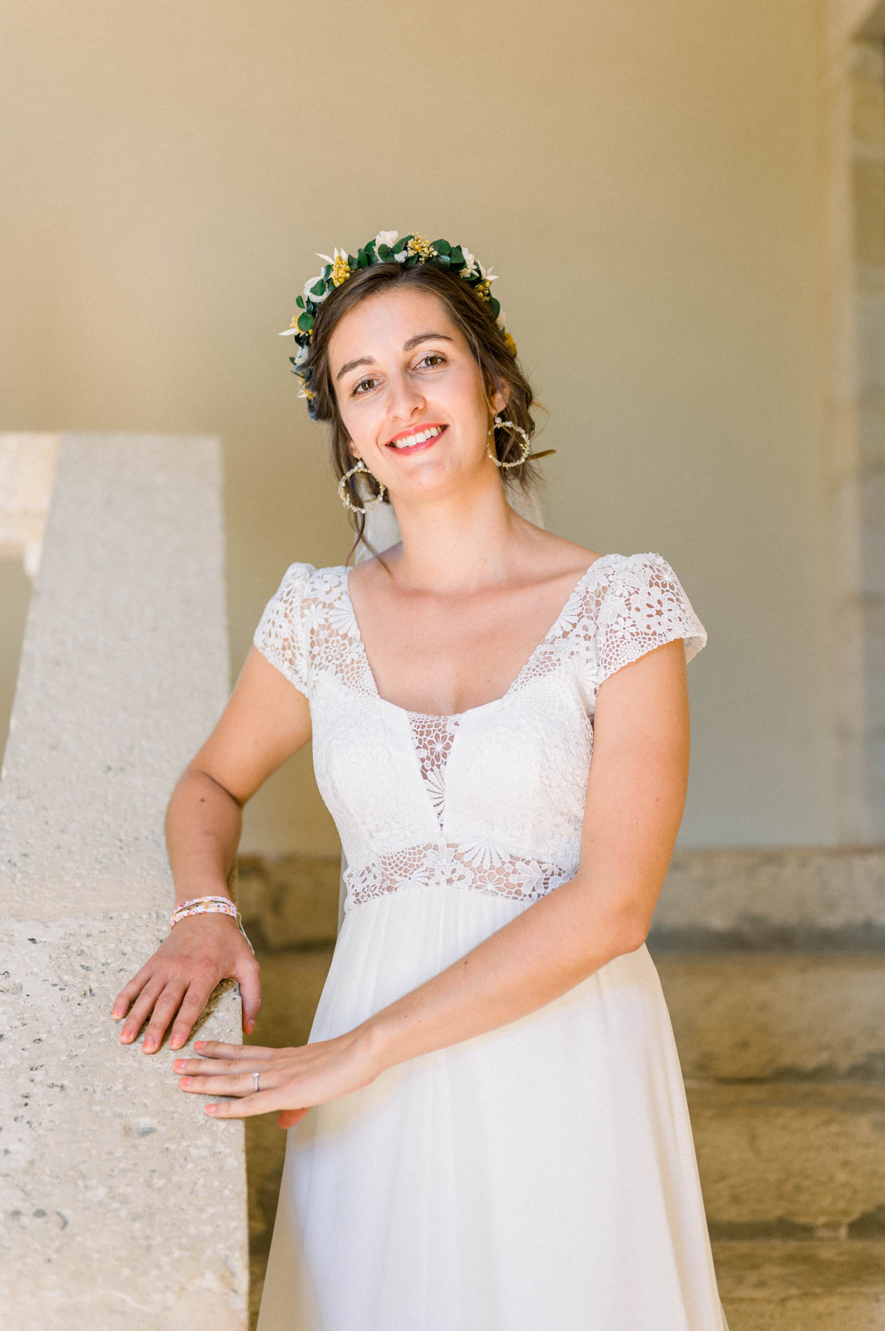 Smiling bride leaning against a stone wall in her lace gown