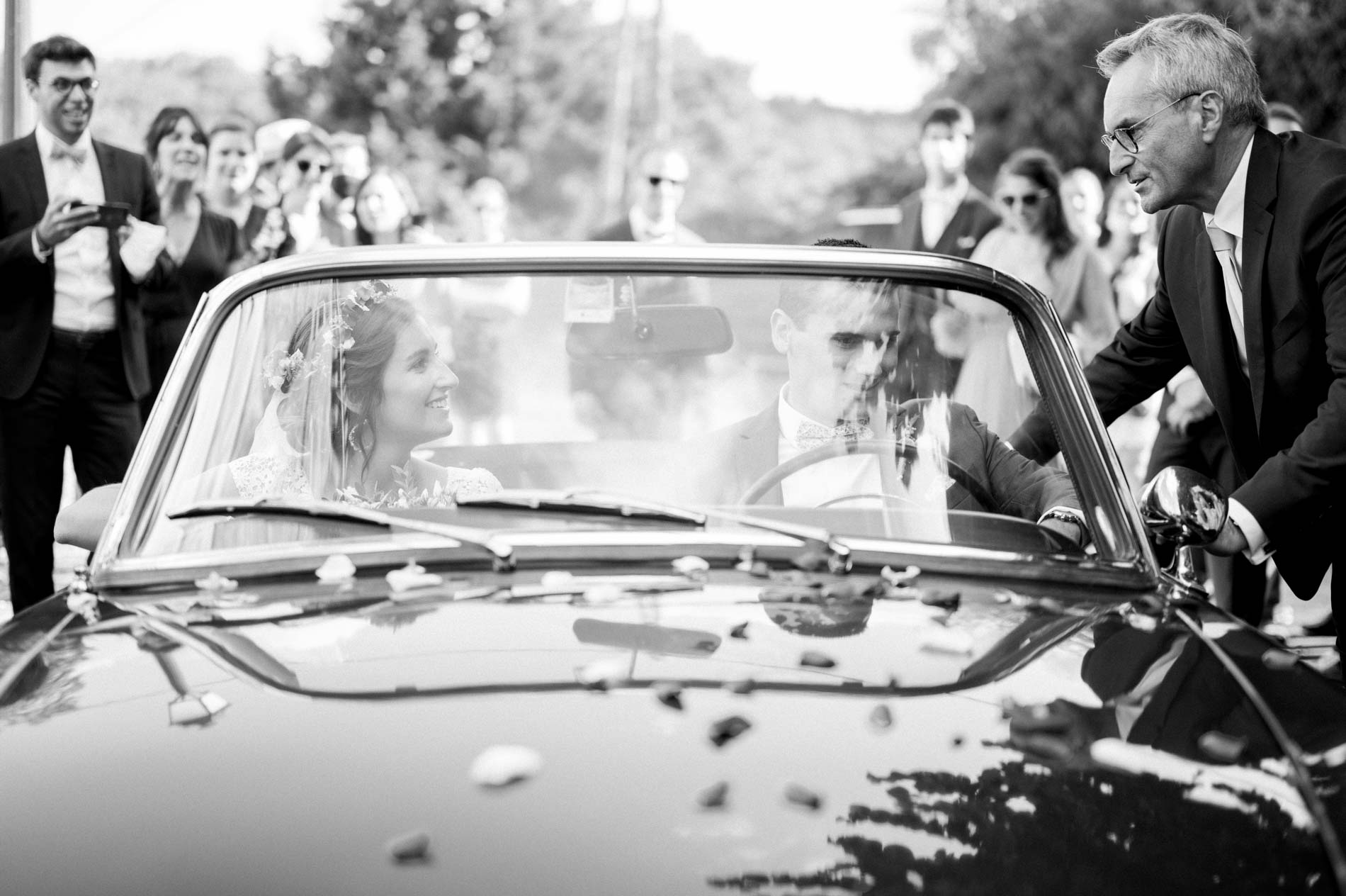 The couple in the convertible as guests cheer, in black and white