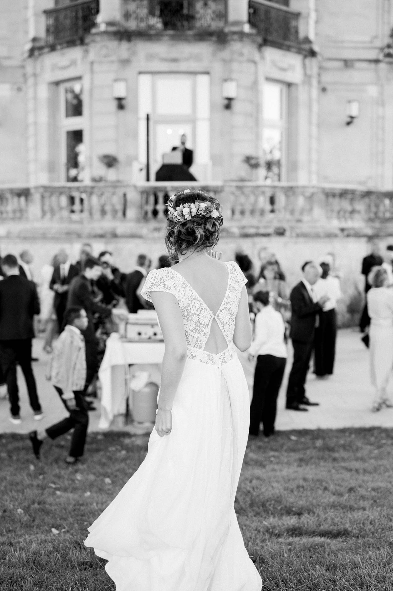Bride seen from behind facing the guests in front of the château, in black and white