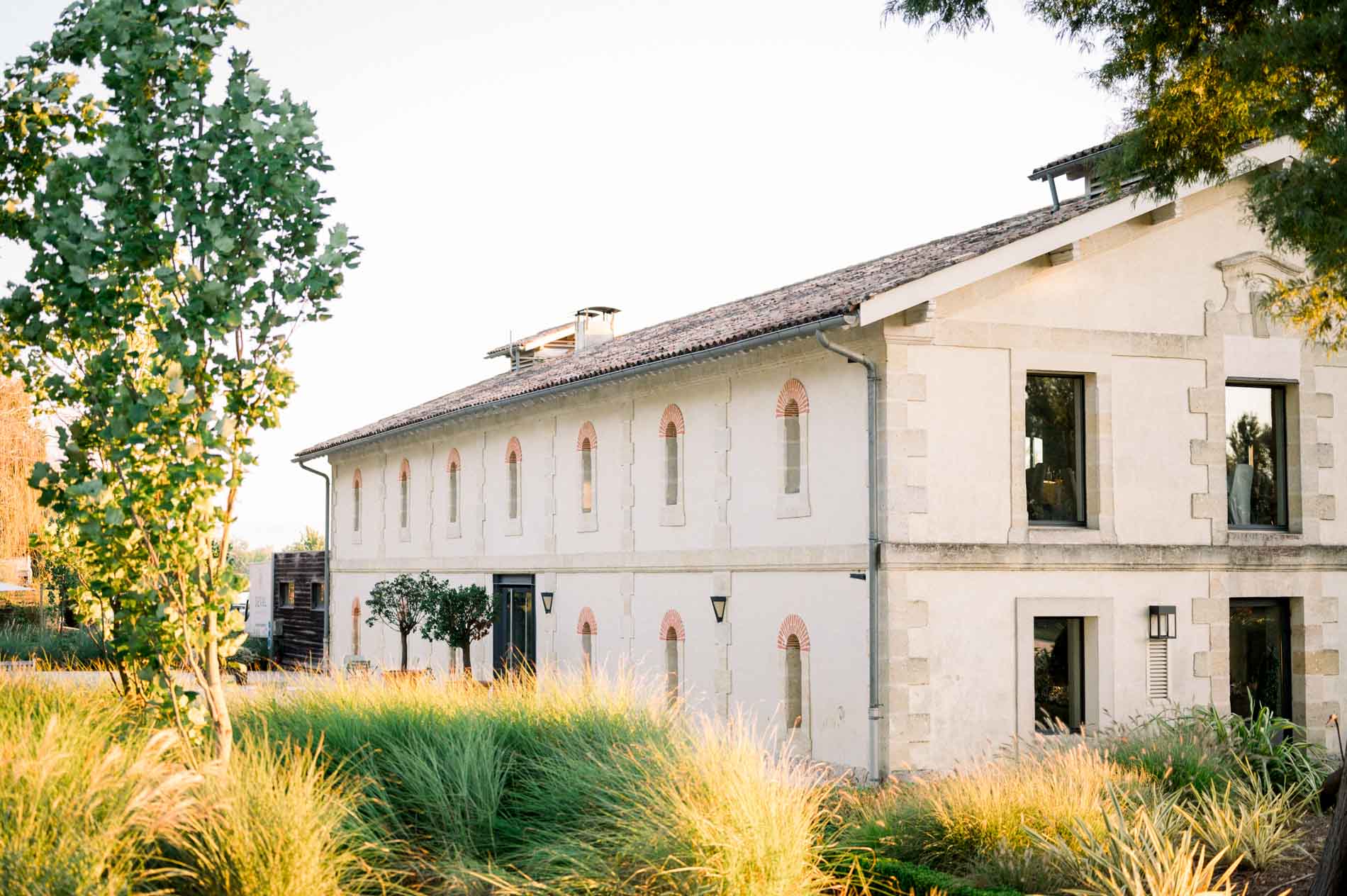 Stone outbuilding of Château Grattequina surrounded by ornamental grasses