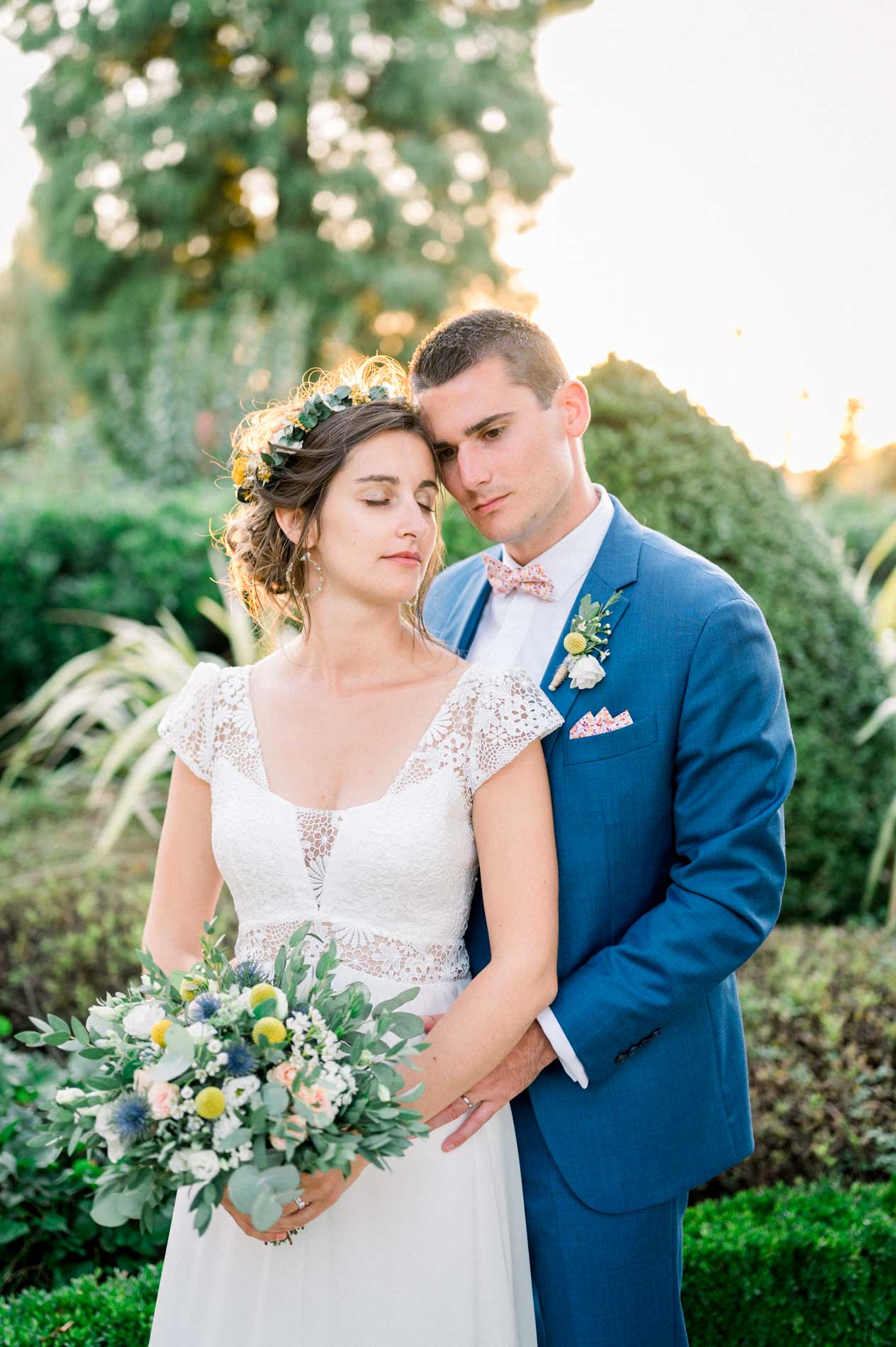 Groom holding the bride, who carries a wildflower bouquet in the garden