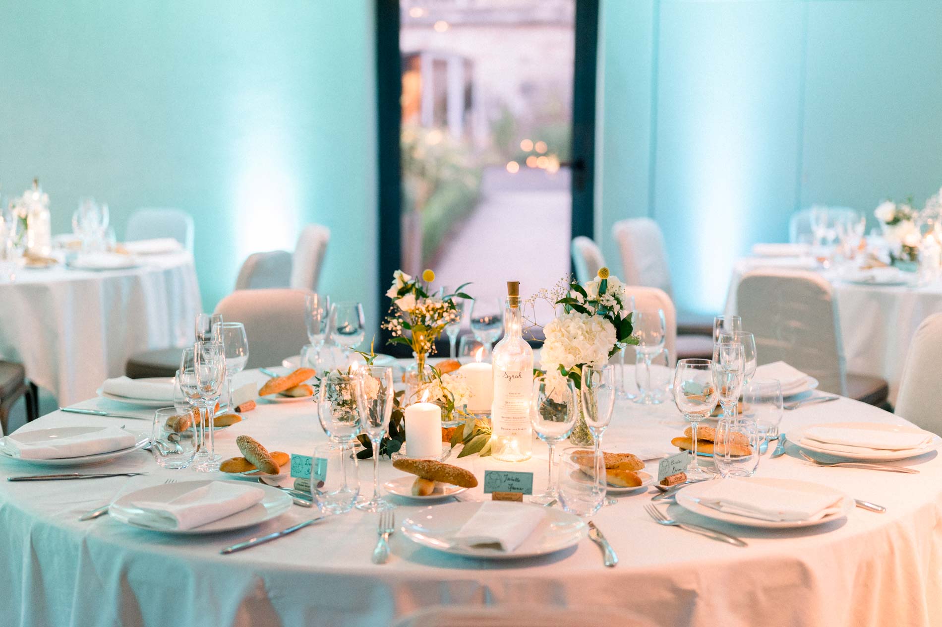 Round table laid with flowers and candles under turquoise lighting