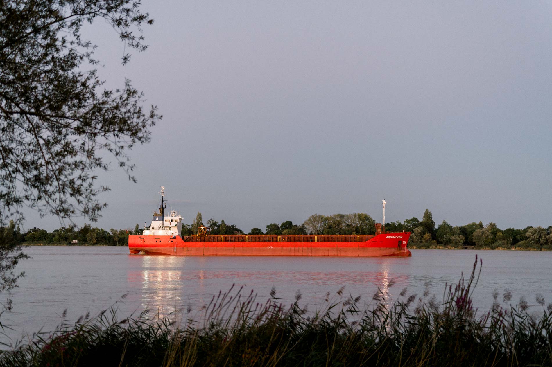 Red cargo ship sailing along the Garonne at dusk