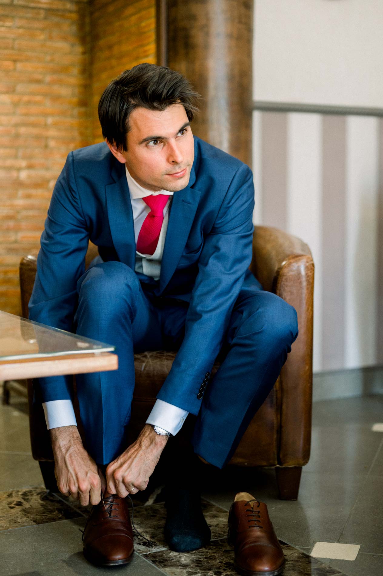 Groom in a blue suit tying his shoes while getting ready at Domaine de Larchey