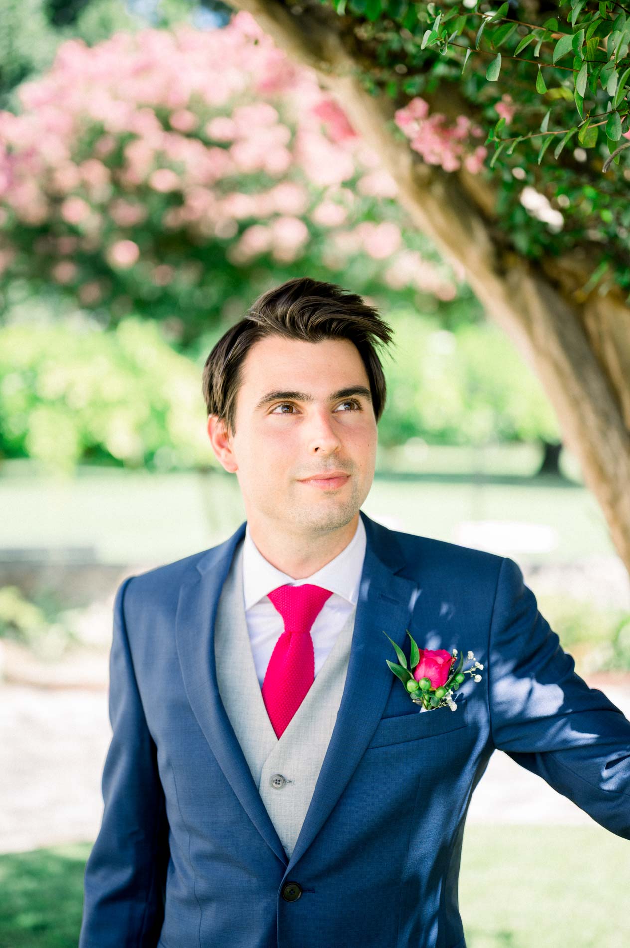 Portrait of the groom in a blue suit, fuchsia tie and boutonniere under a flowering tree