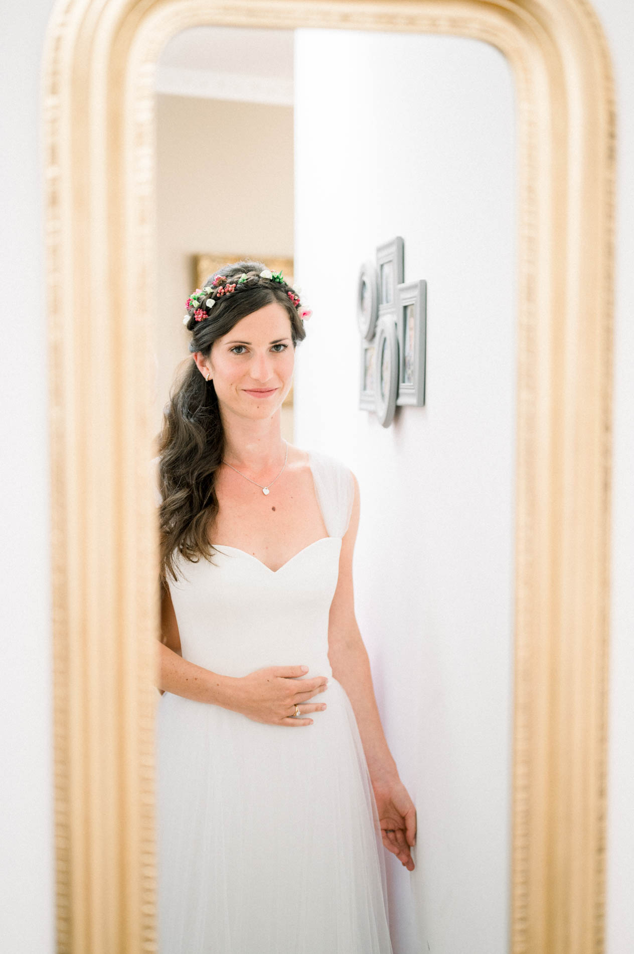 Bride in her lace gown reflected in a tall gilded mirror