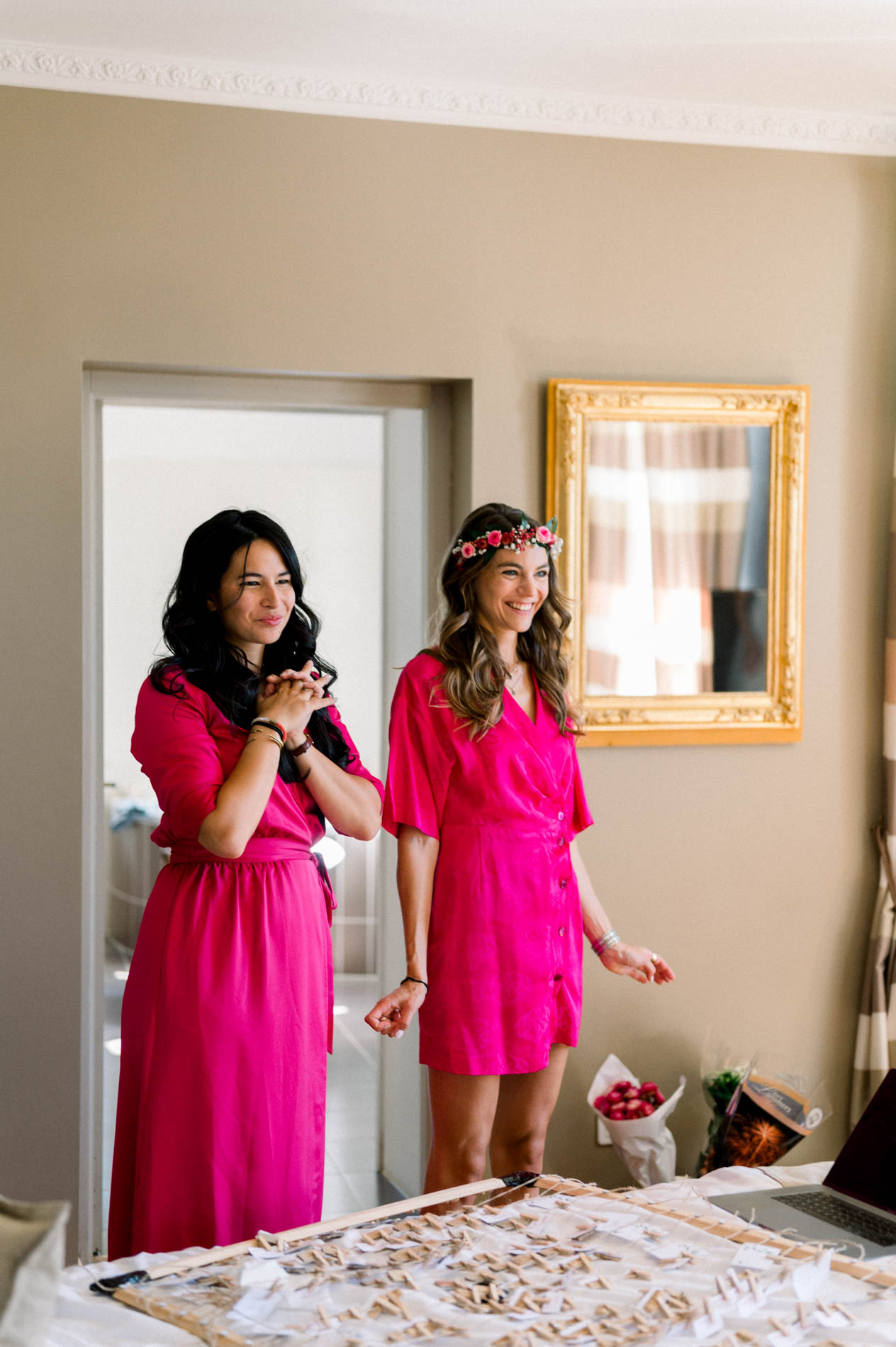 Two bridesmaids in fuchsia dresses seeing the bride for the first time while getting ready