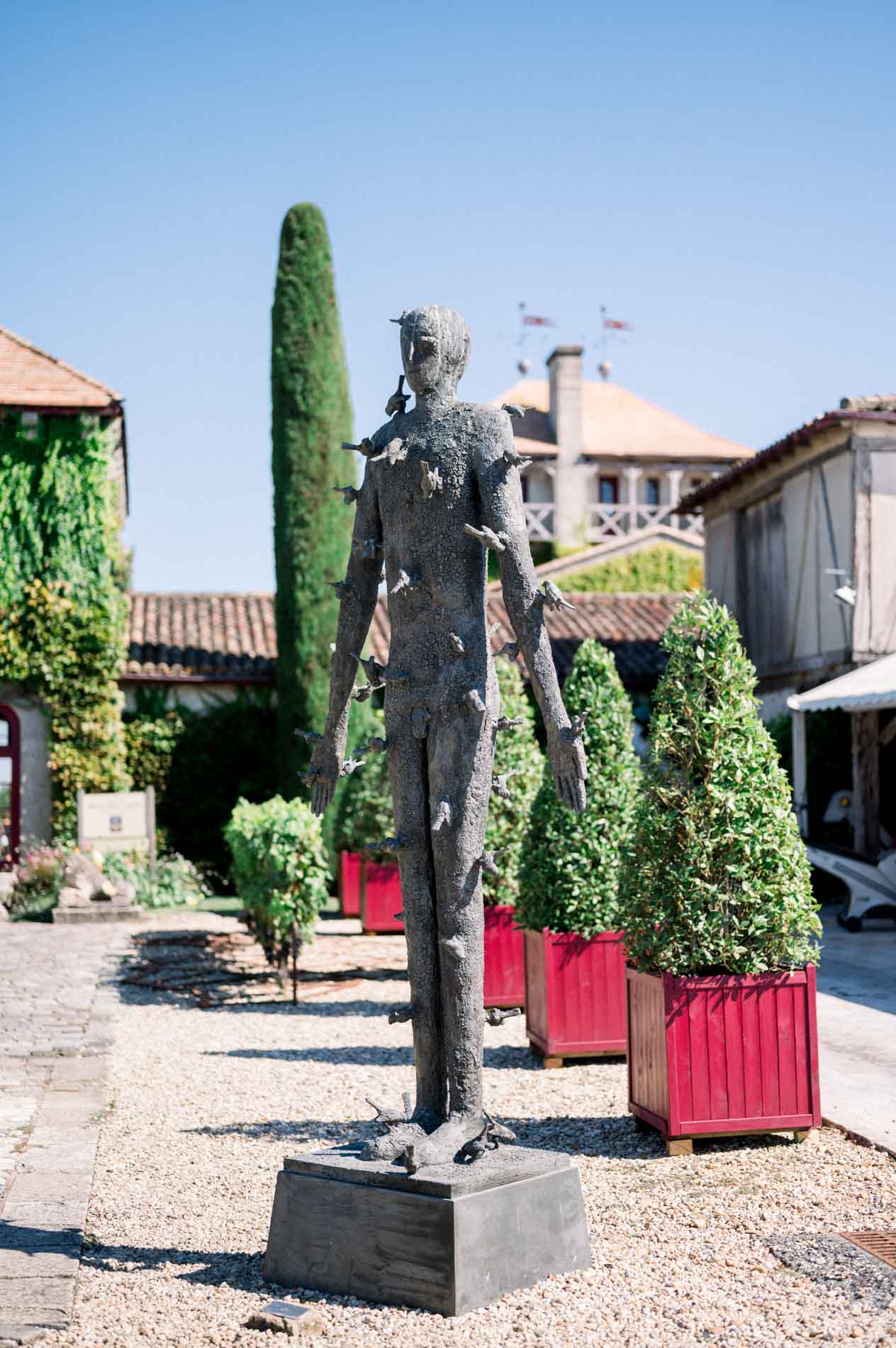 Bronze statue in the courtyard of Château Smith Haut Lafitte among cypresses and red planters