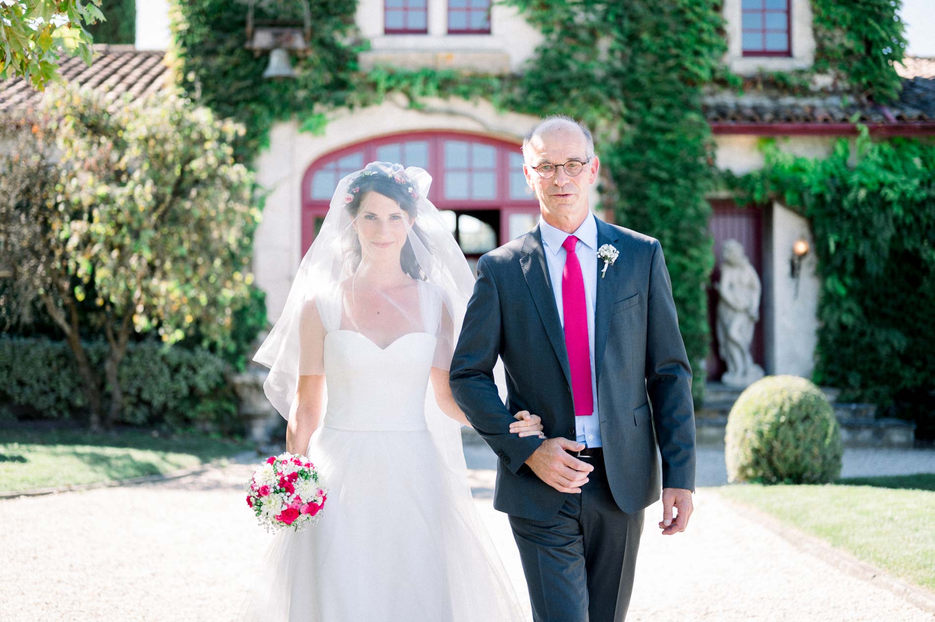 The bride walks into the ceremony on the arm of a loved one, in front of the château