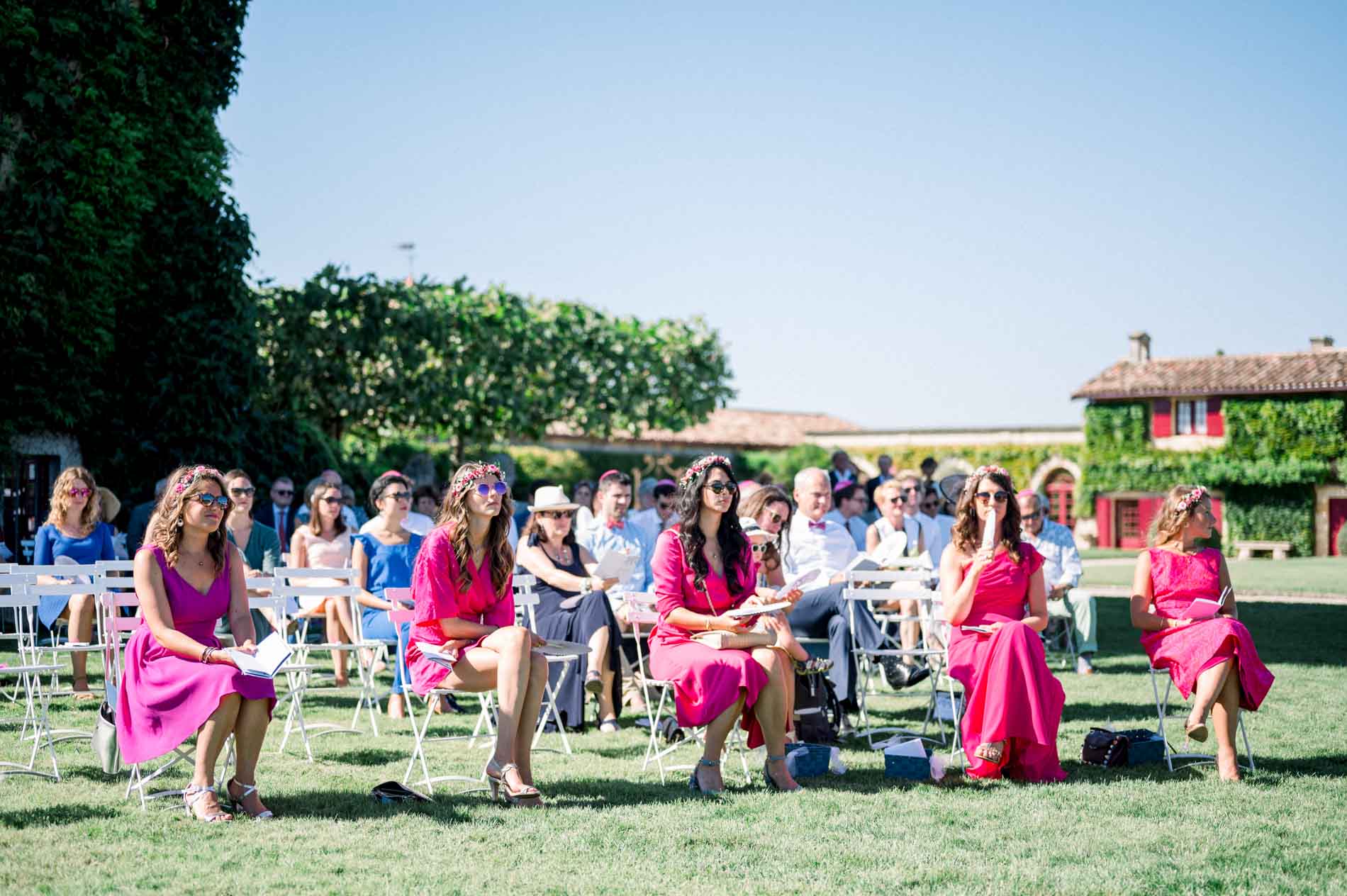 Guests in fuchsia dresses seated on the lawn during the wedding ceremony