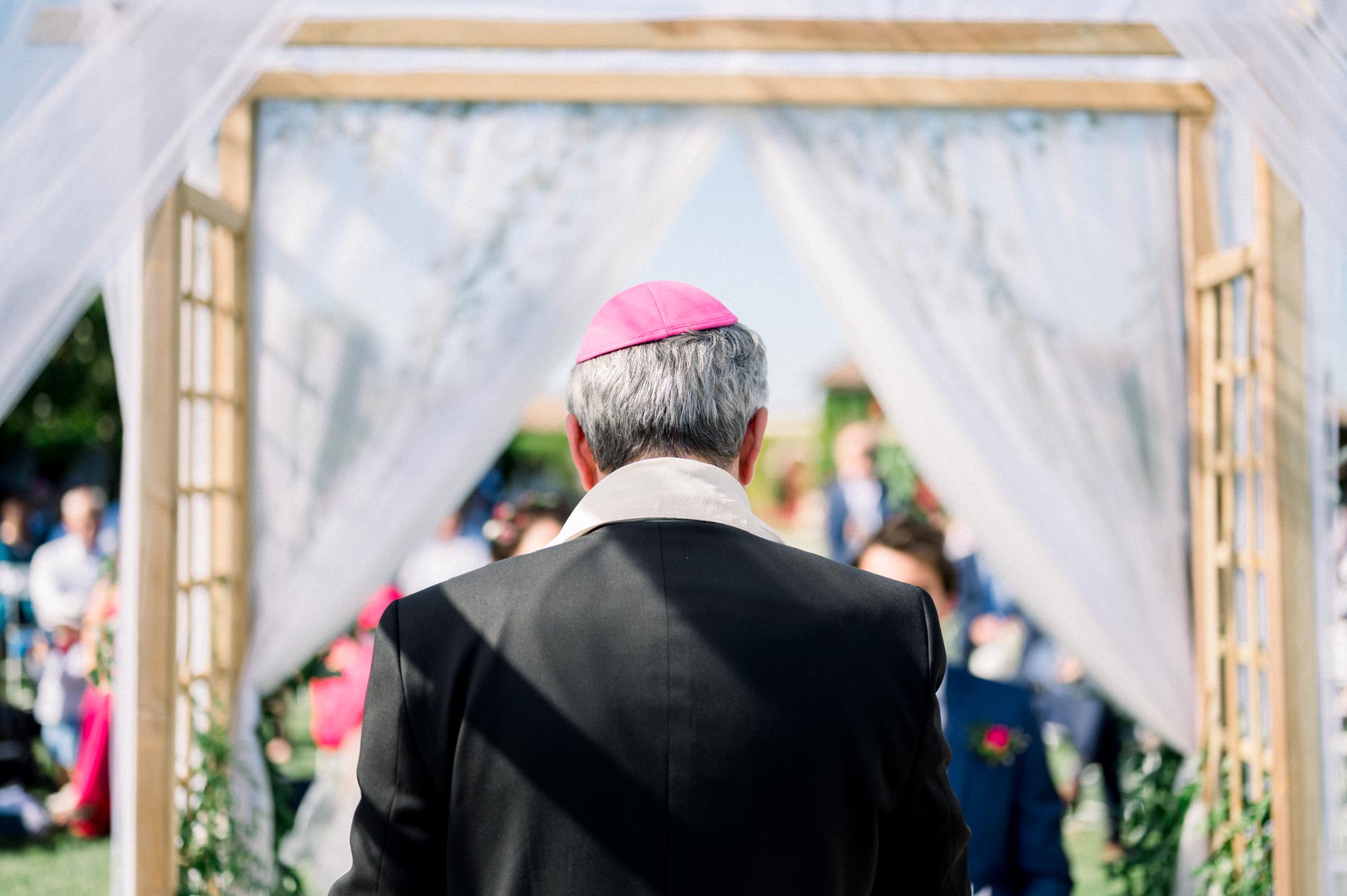 The officiant seen from behind, wearing a pink kippah, facing the ceremony arch