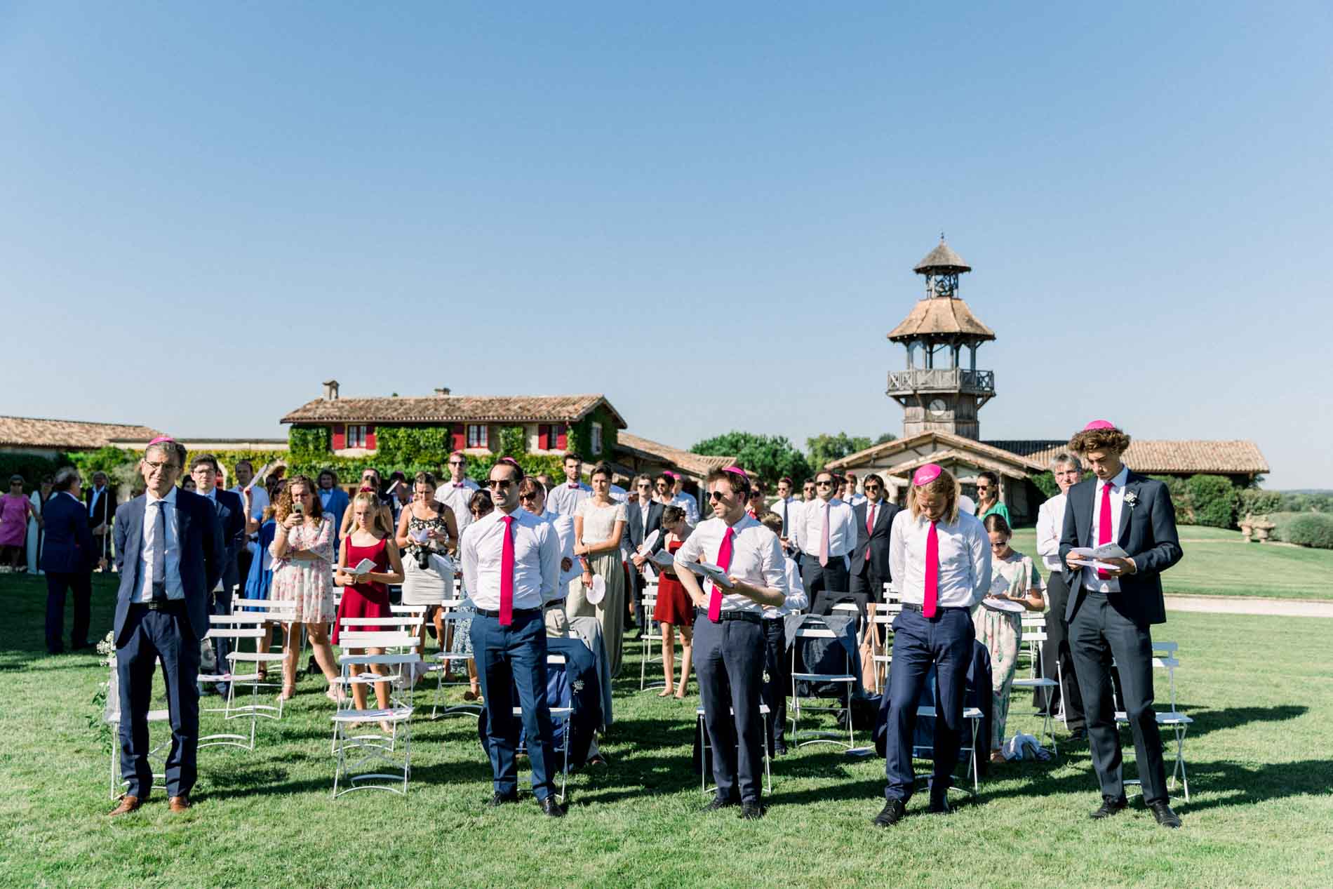 Groomsmen in pink ties standing on the lawn in front of the château tower