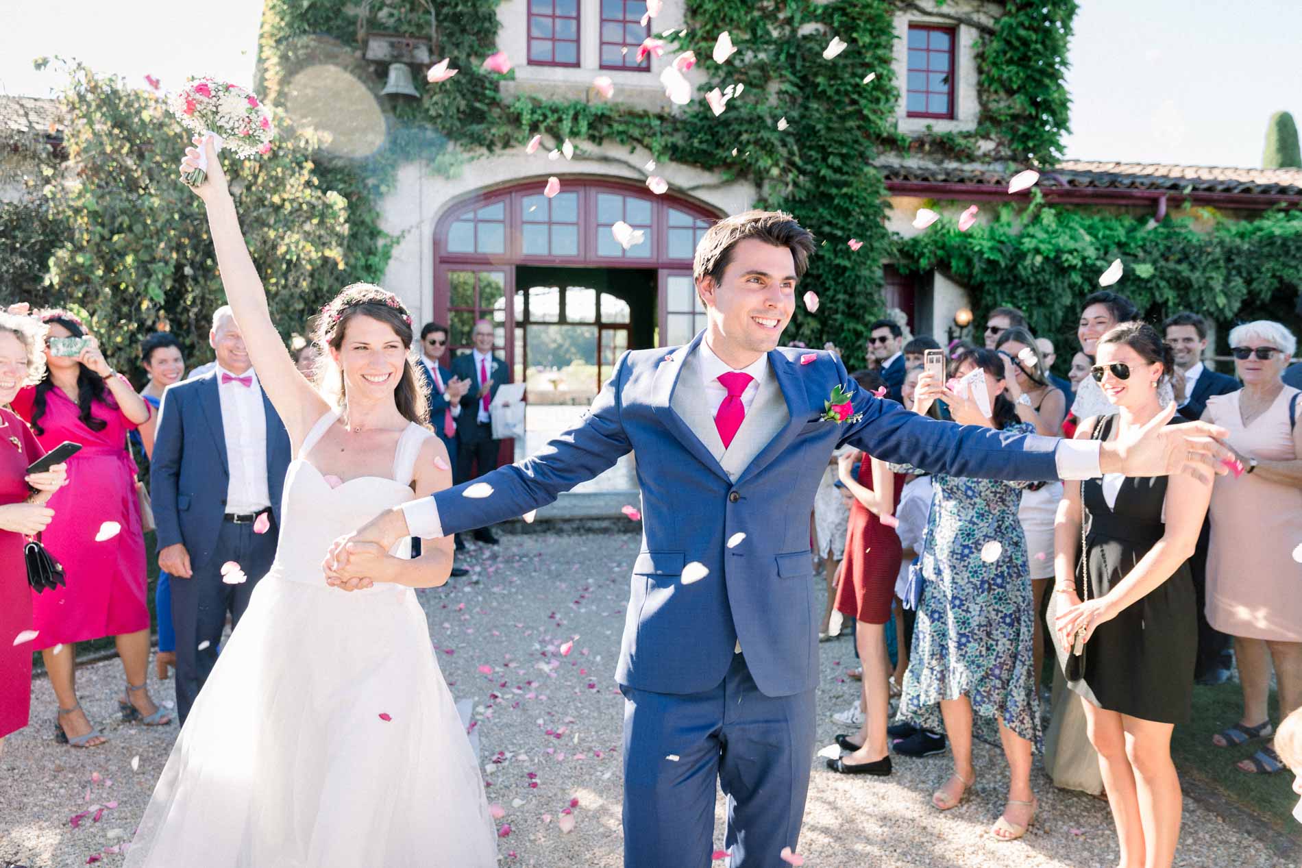 The newlyweds exit under a shower of petals, cheered by their guests outside the château