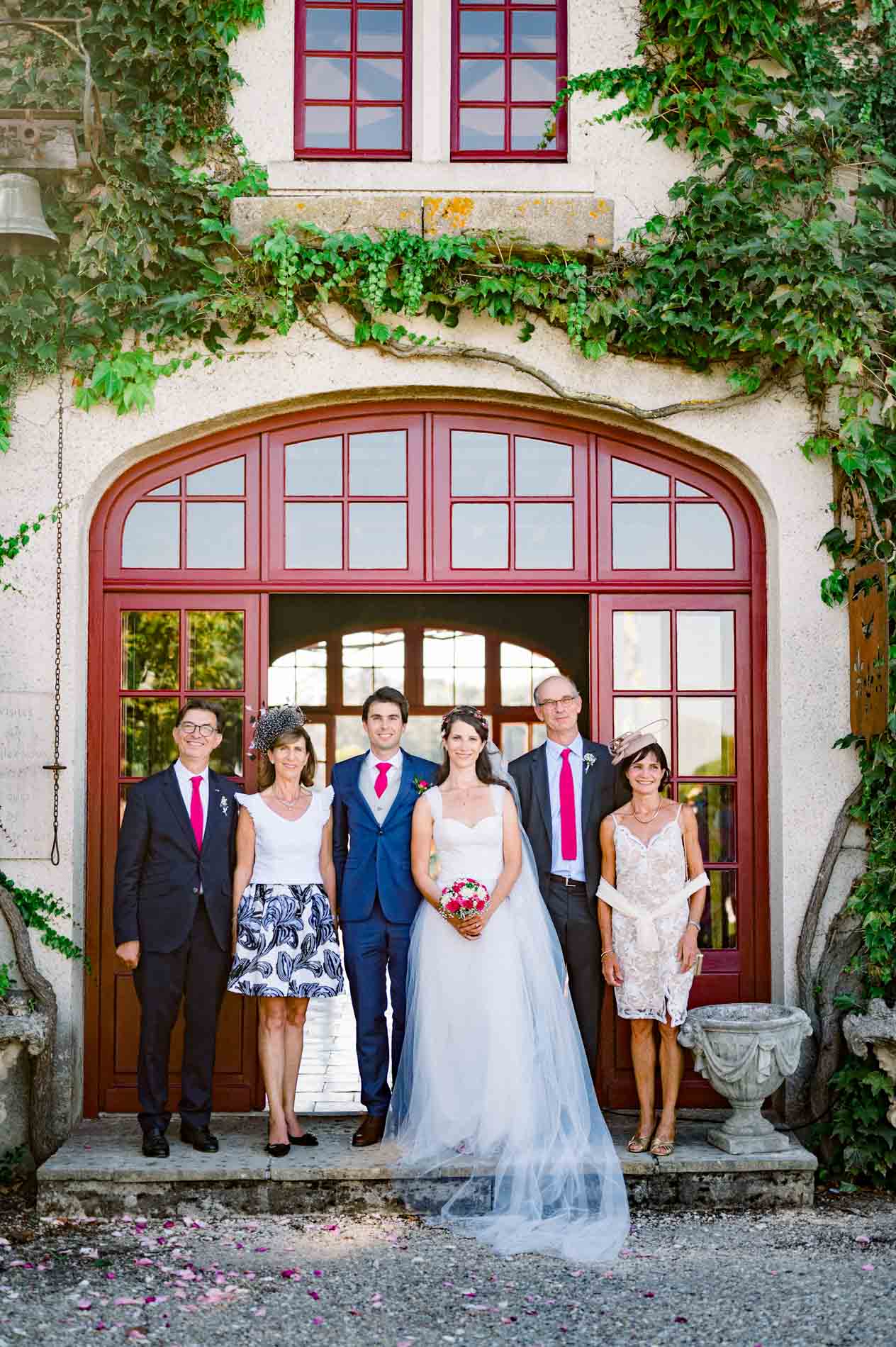 Family photo with the newlyweds in front of the ivy-framed red arched door