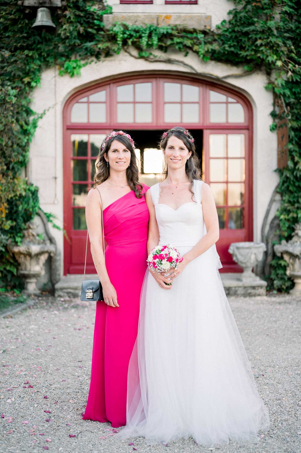 The bride and her bridesmaid in a fuchsia dress in front of the red arched door