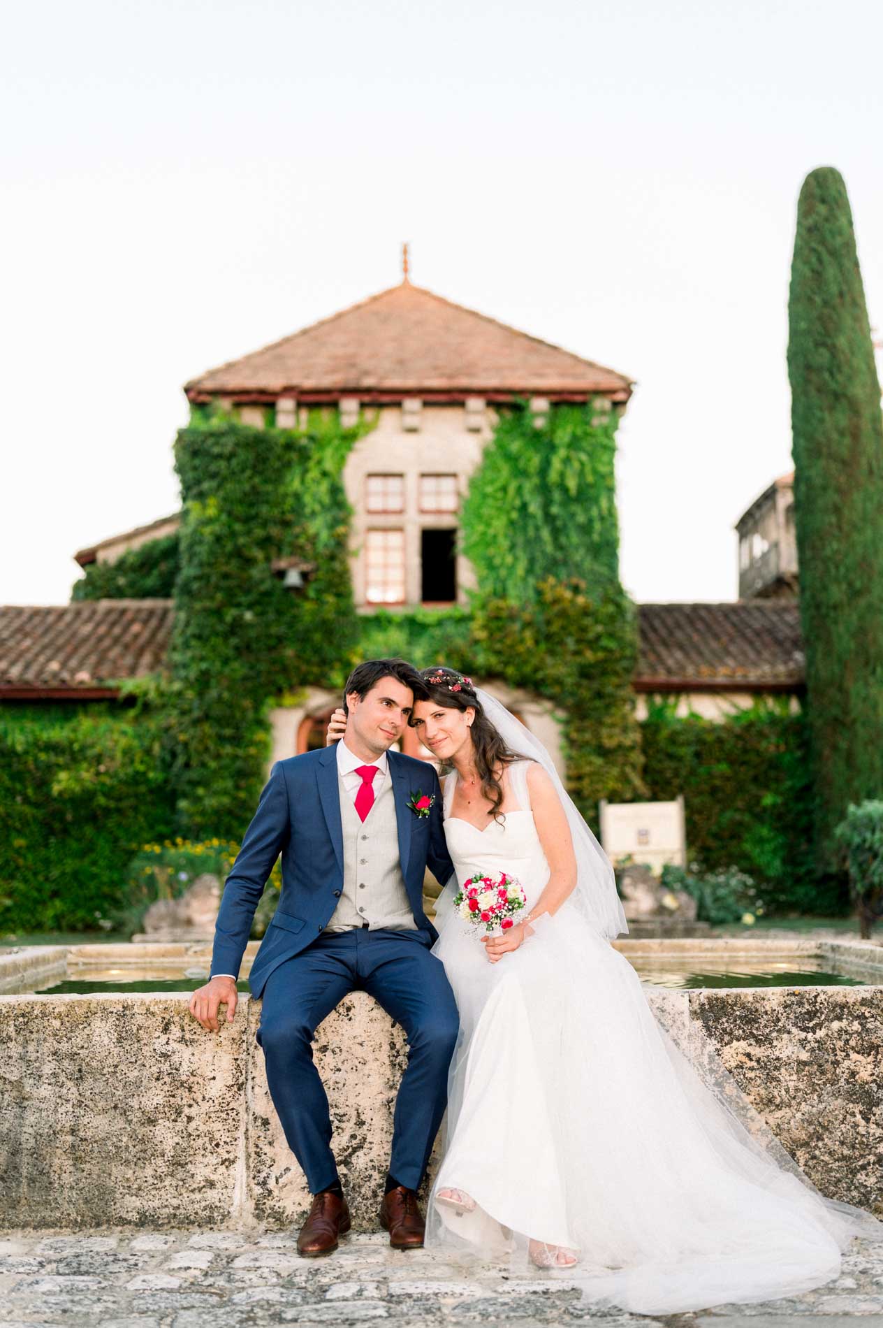 The bride and groom sitting on a stone wall in front of the ivy-covered building
