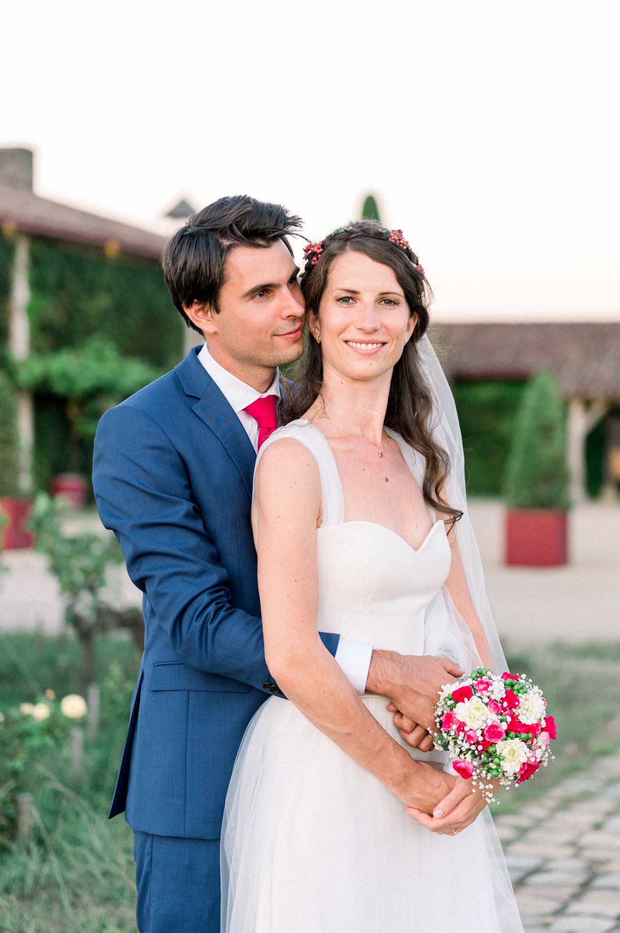 The groom holds the bride from behind as she carries her rose bouquet