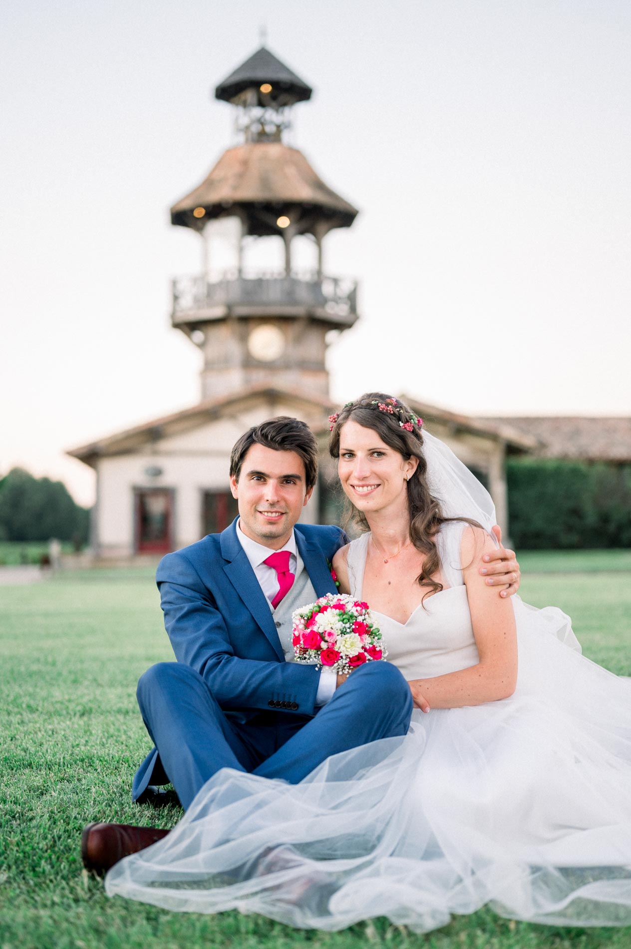 The newlyweds sitting on the grass in front of the château's belvedere tower