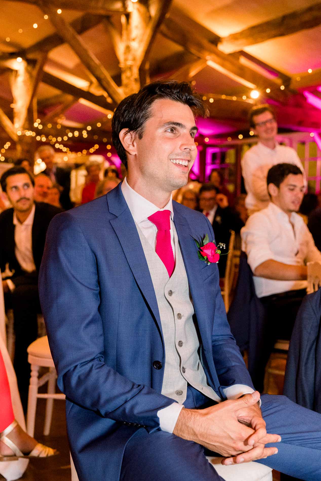 The groom seated and smiling during dinner beneath string lights