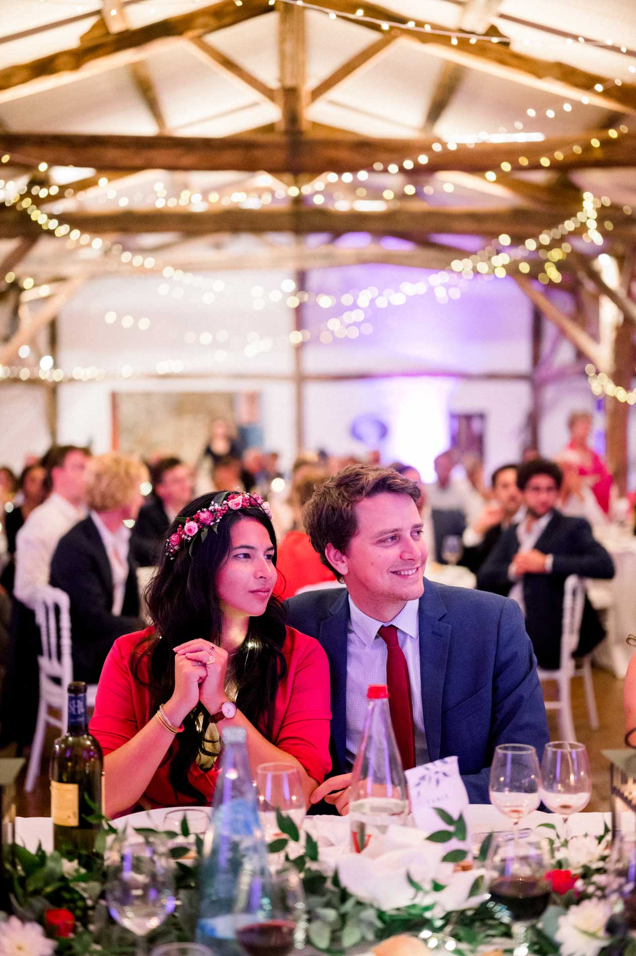 Guests seated at their table beneath the string lights of the reception hall