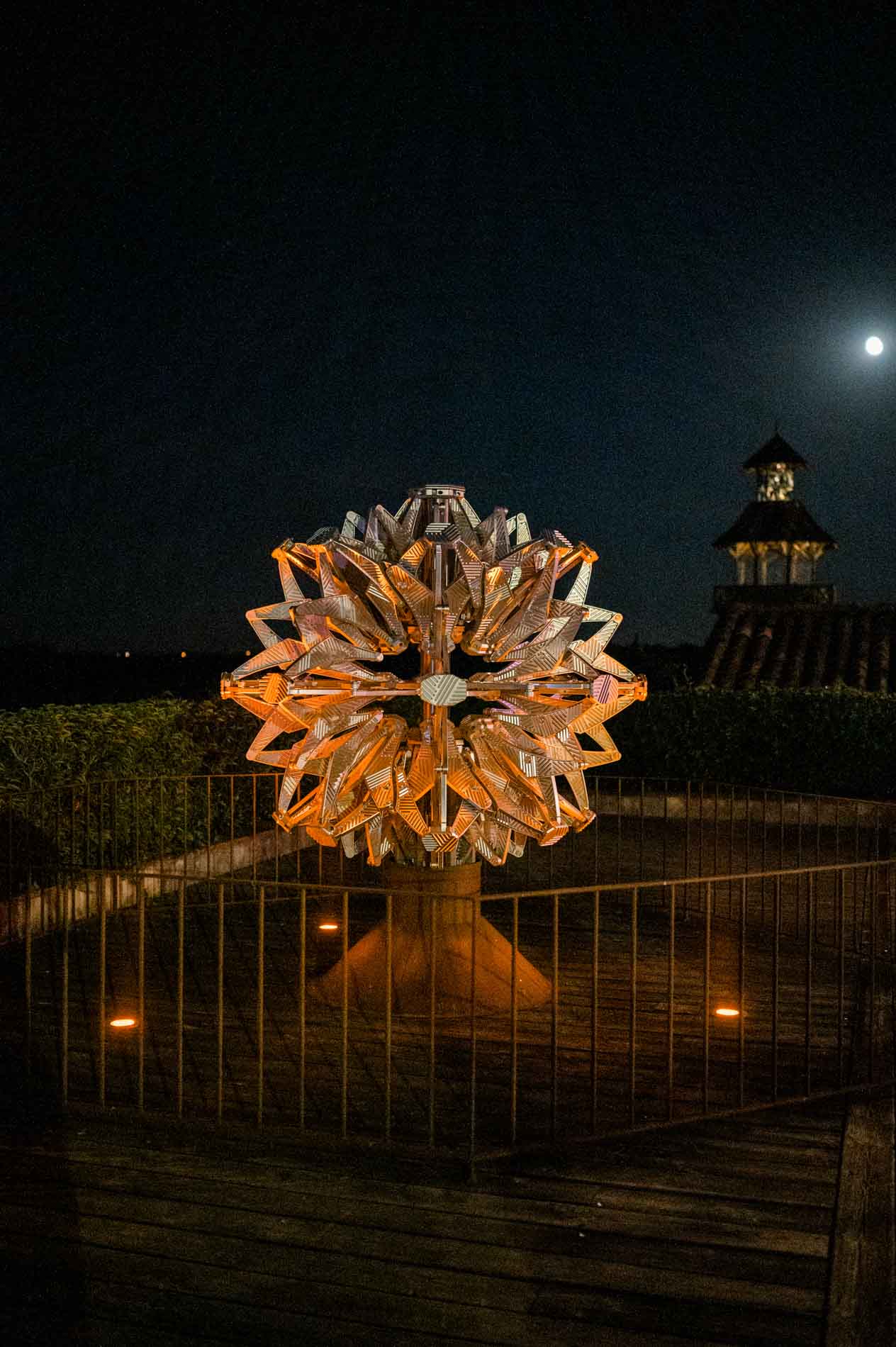 Illuminated metal sculpture on the terrace at night, with the tower in the distance