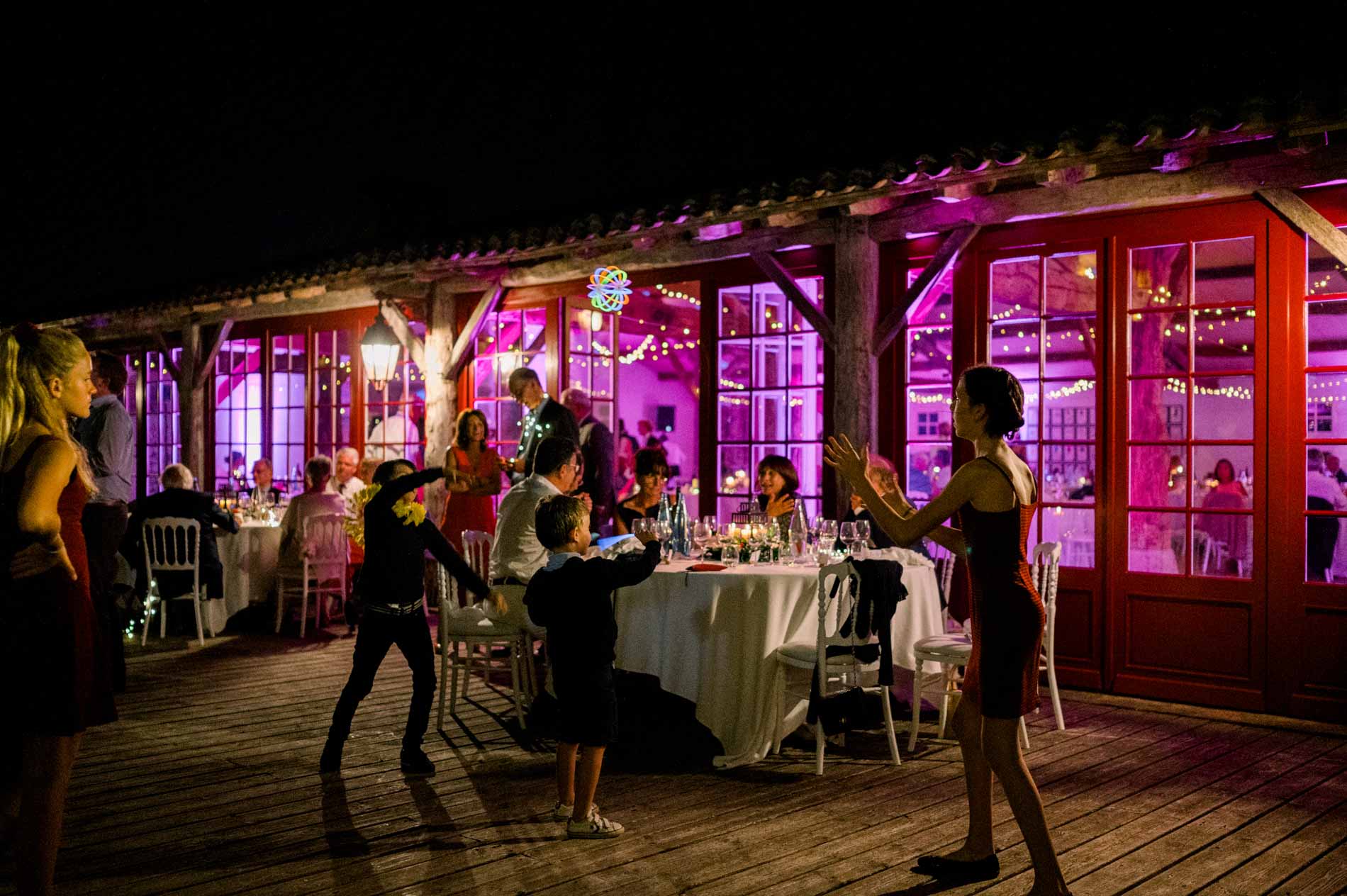 The reception hall terrace lit in pink at night, with guests outside