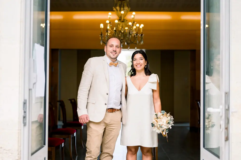 The couple on the threshold of the wedding room beneath a gilded chandelier