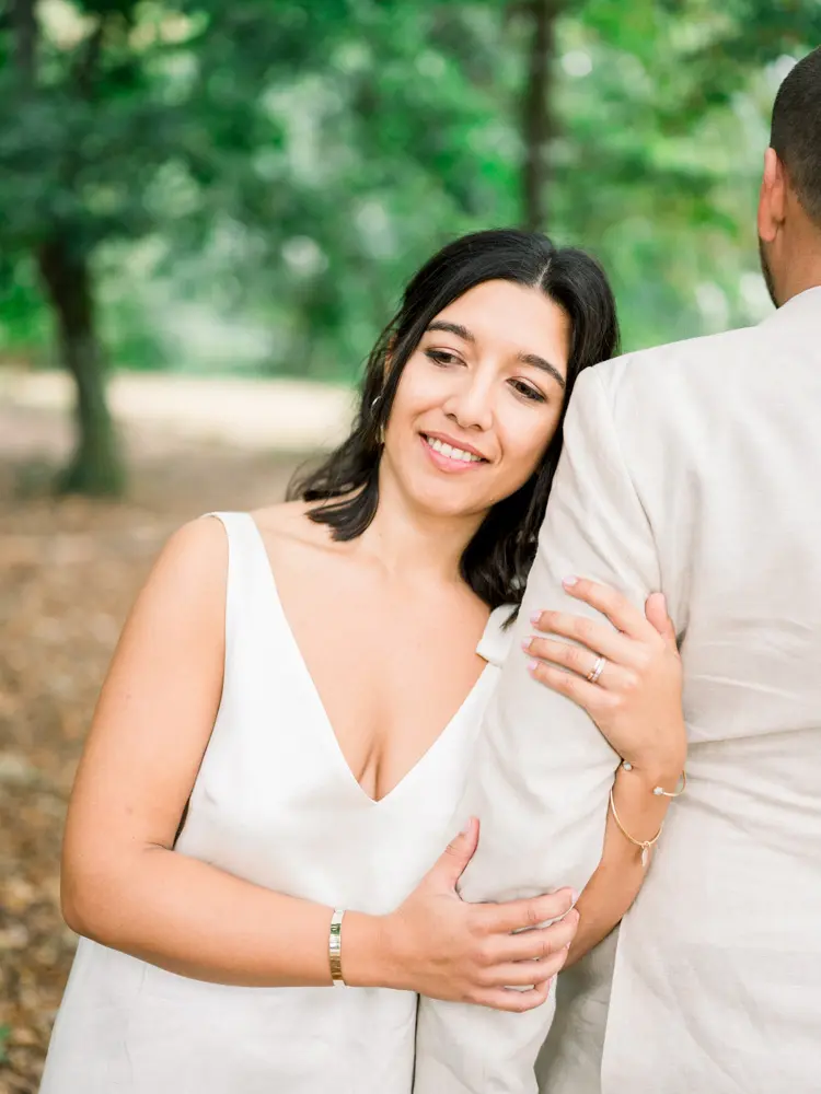 The smiling bride holding the groom's arm in the woods