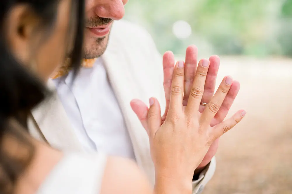 The couple's hands meeting, wedding rings on their fingers, in the foreground